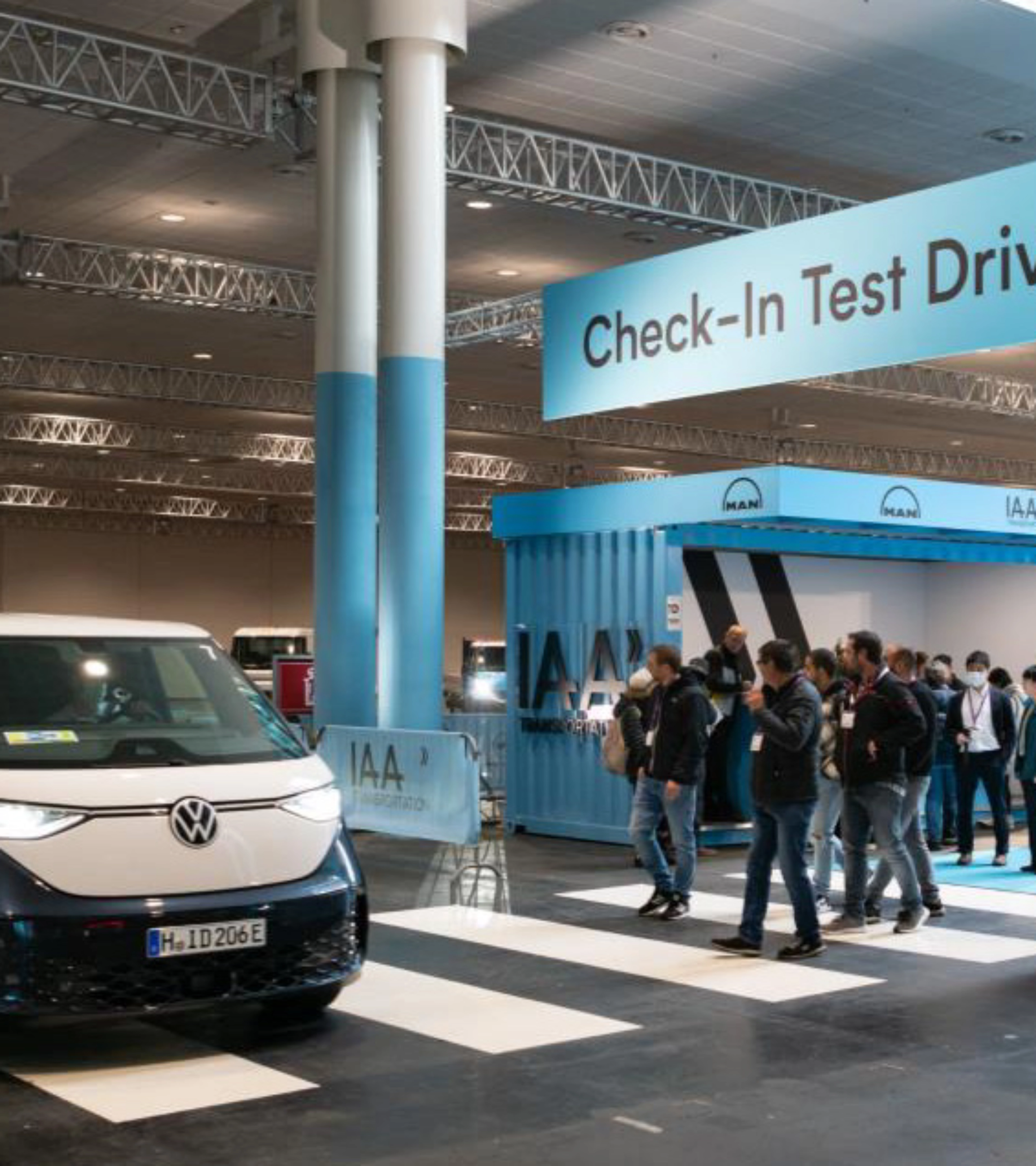 Exhibition hall scene with a Volkswagen van driving past the IAA Transportation check-in for test drives.