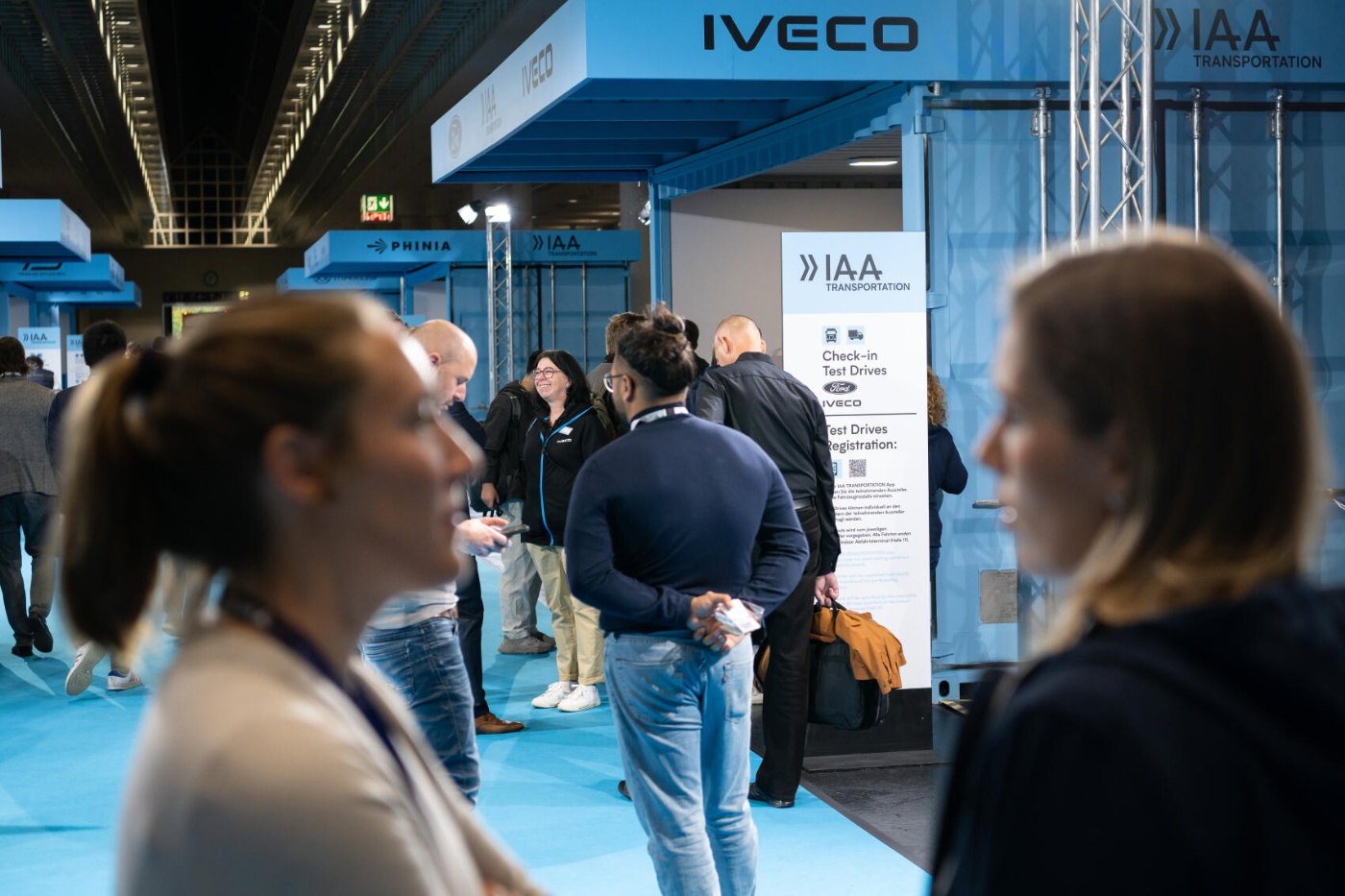 Personen gehen durch eine IAA‑Transportation‑Halle mit Ausstellungsständen auf beiden Seiten.