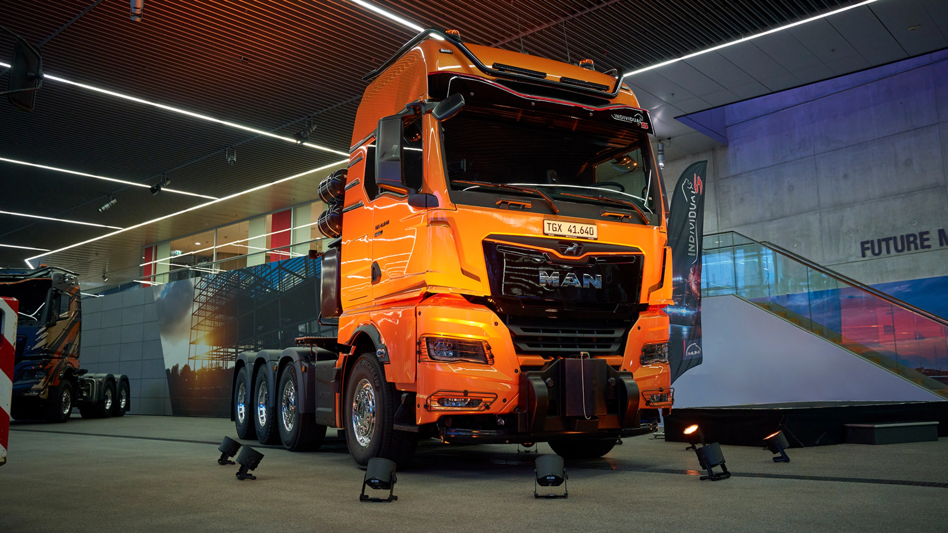 Orange MAN TGX 41.640 truck displayed at an indoor exhibition.