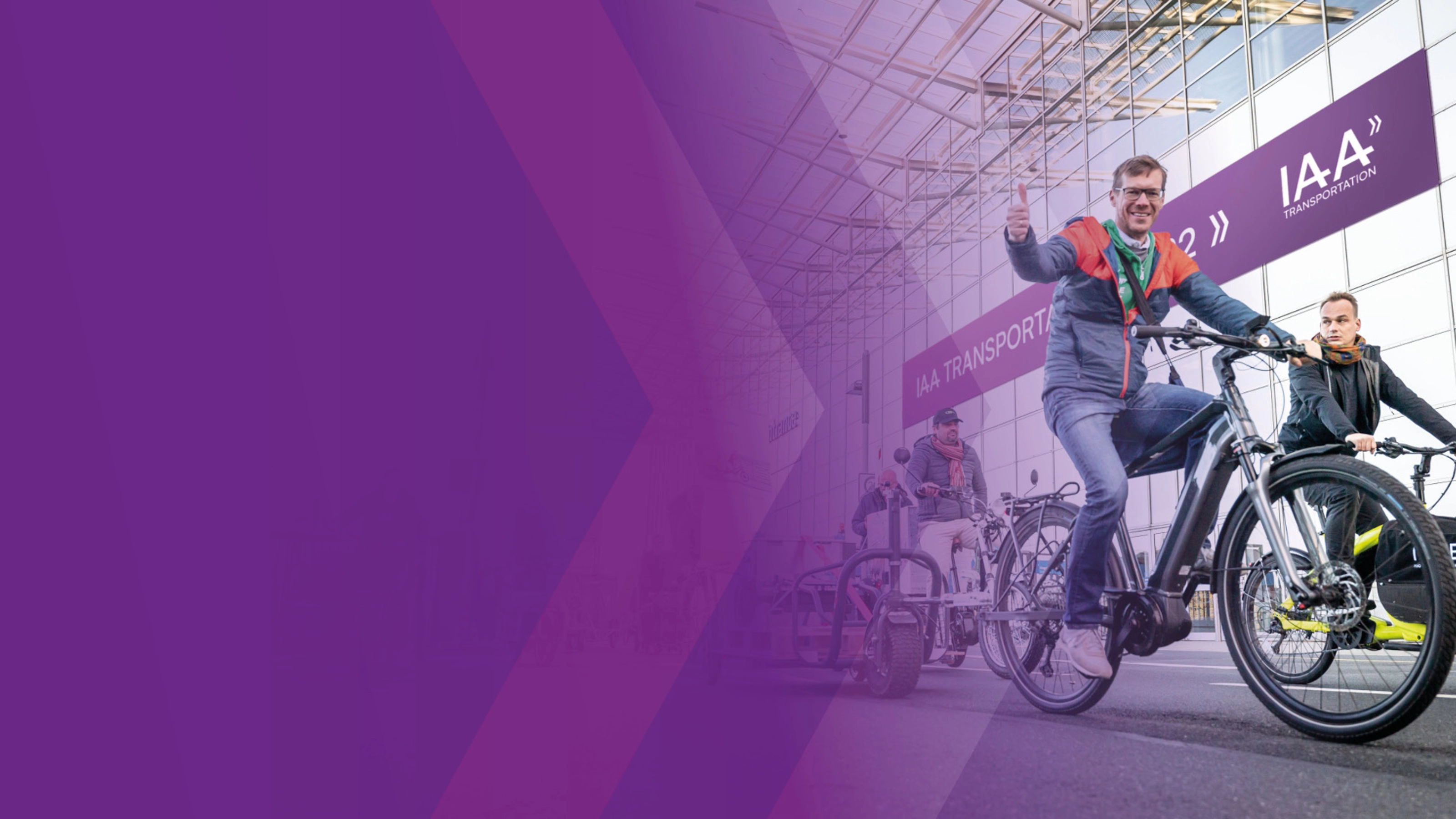 Man riding an e-bike and giving a thumbs up at a trade fair entrance.