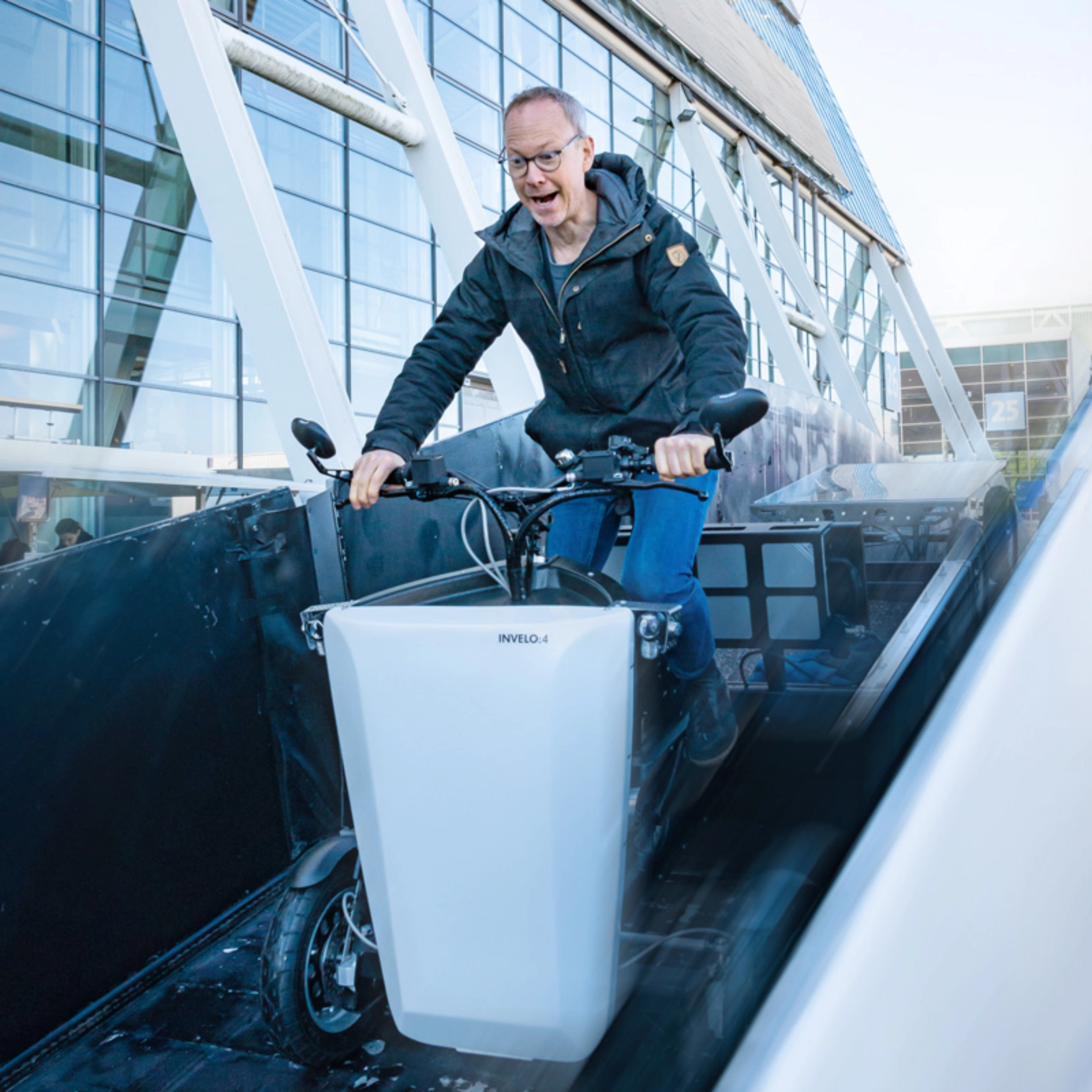 A person rides a cargo bike outside a hall with glass panels at the IAA Transportation.