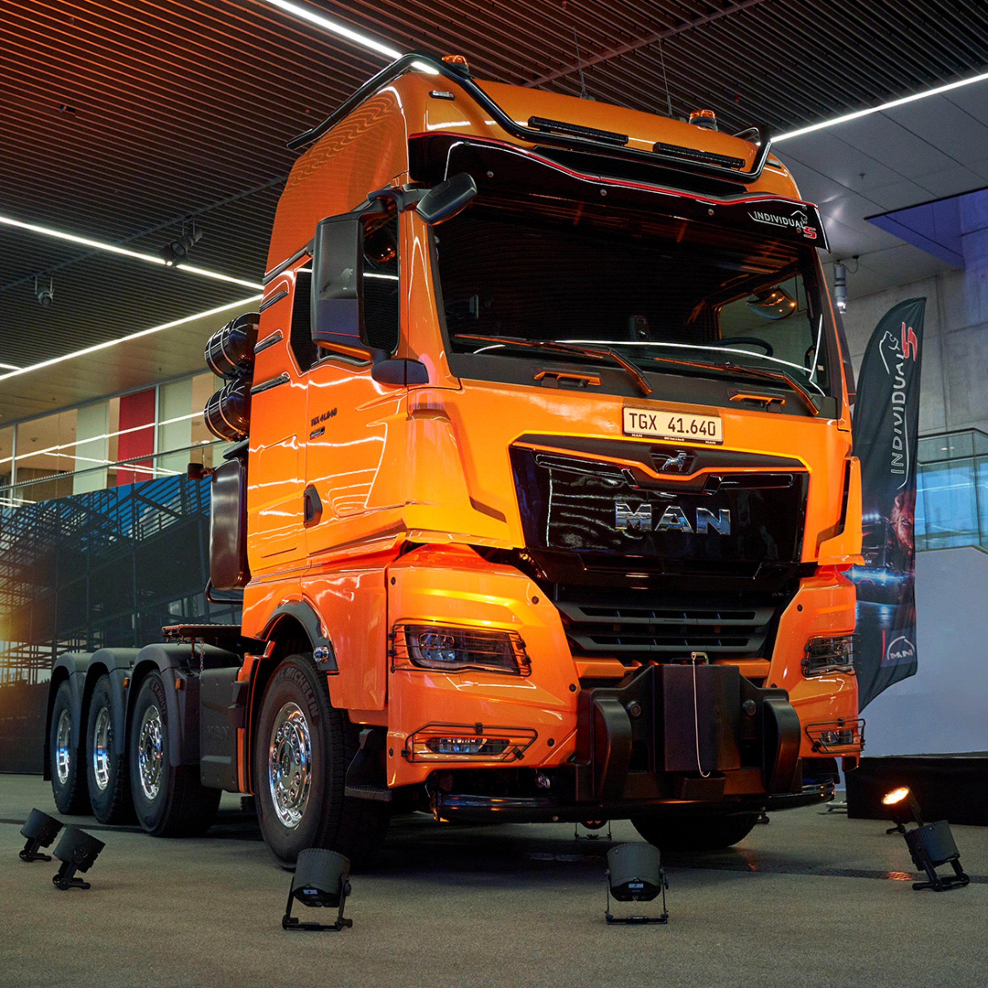 Orange MAN TGX 41.640 truck displayed at an indoor exhibition.