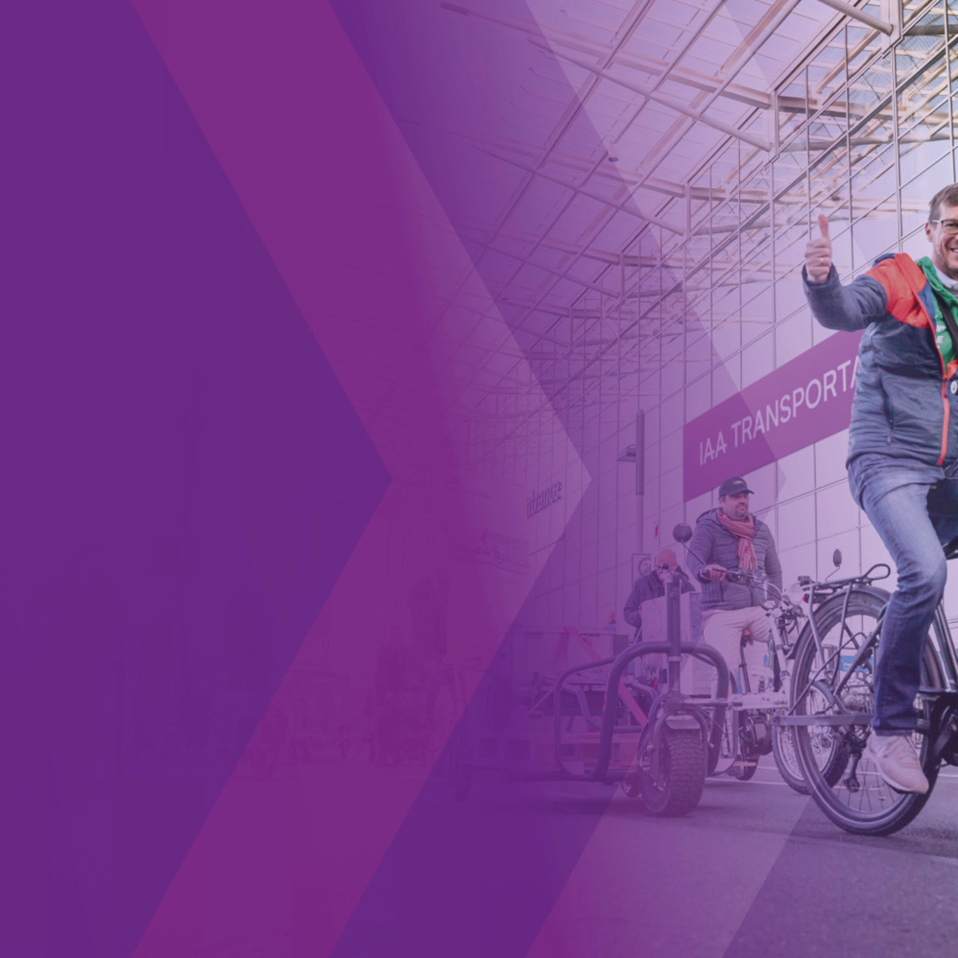 Man riding an e-bike and giving a thumbs up at a trade fair entrance.