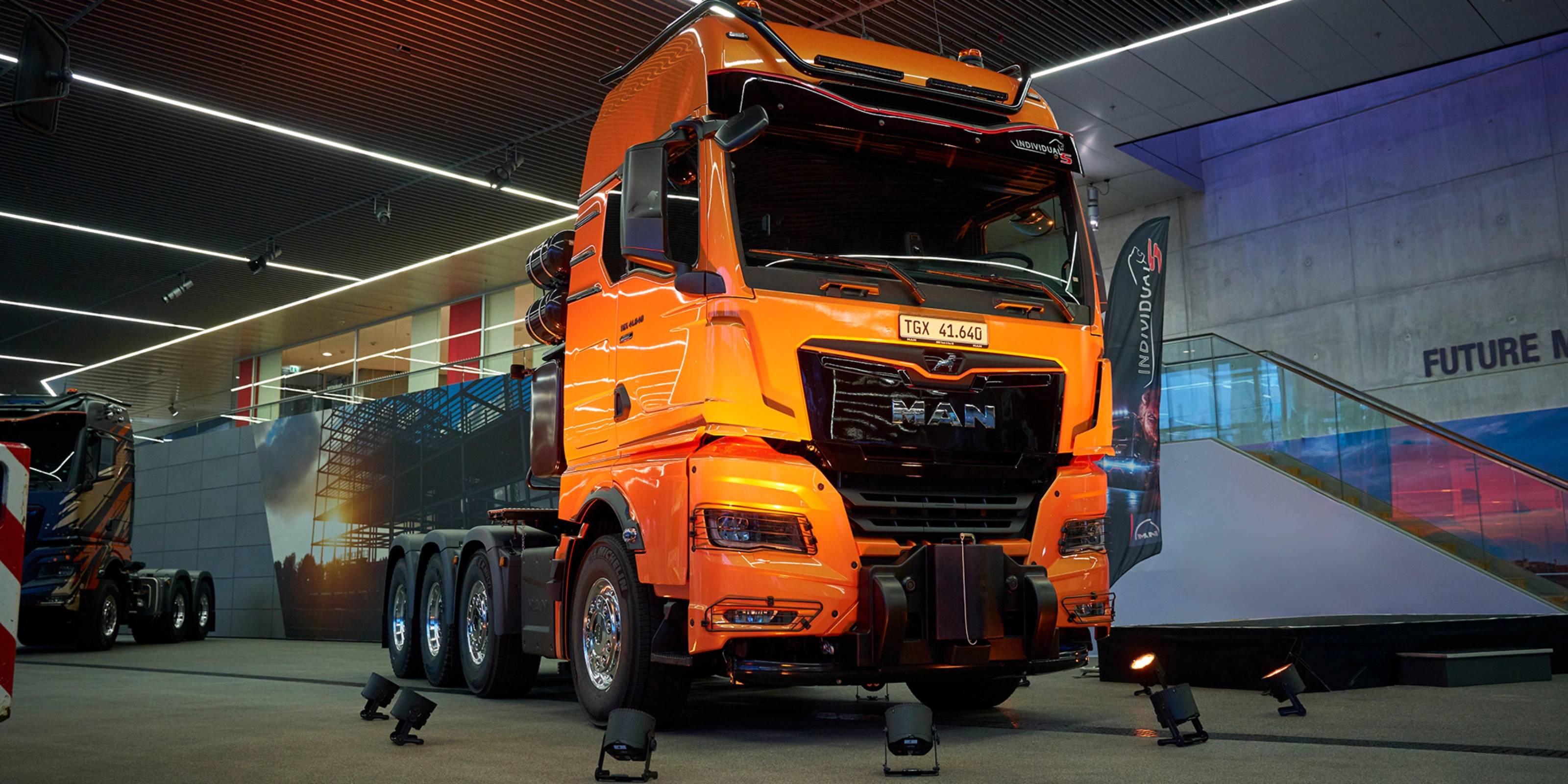 Orange MAN TGX 41.640 truck displayed at an indoor exhibition.