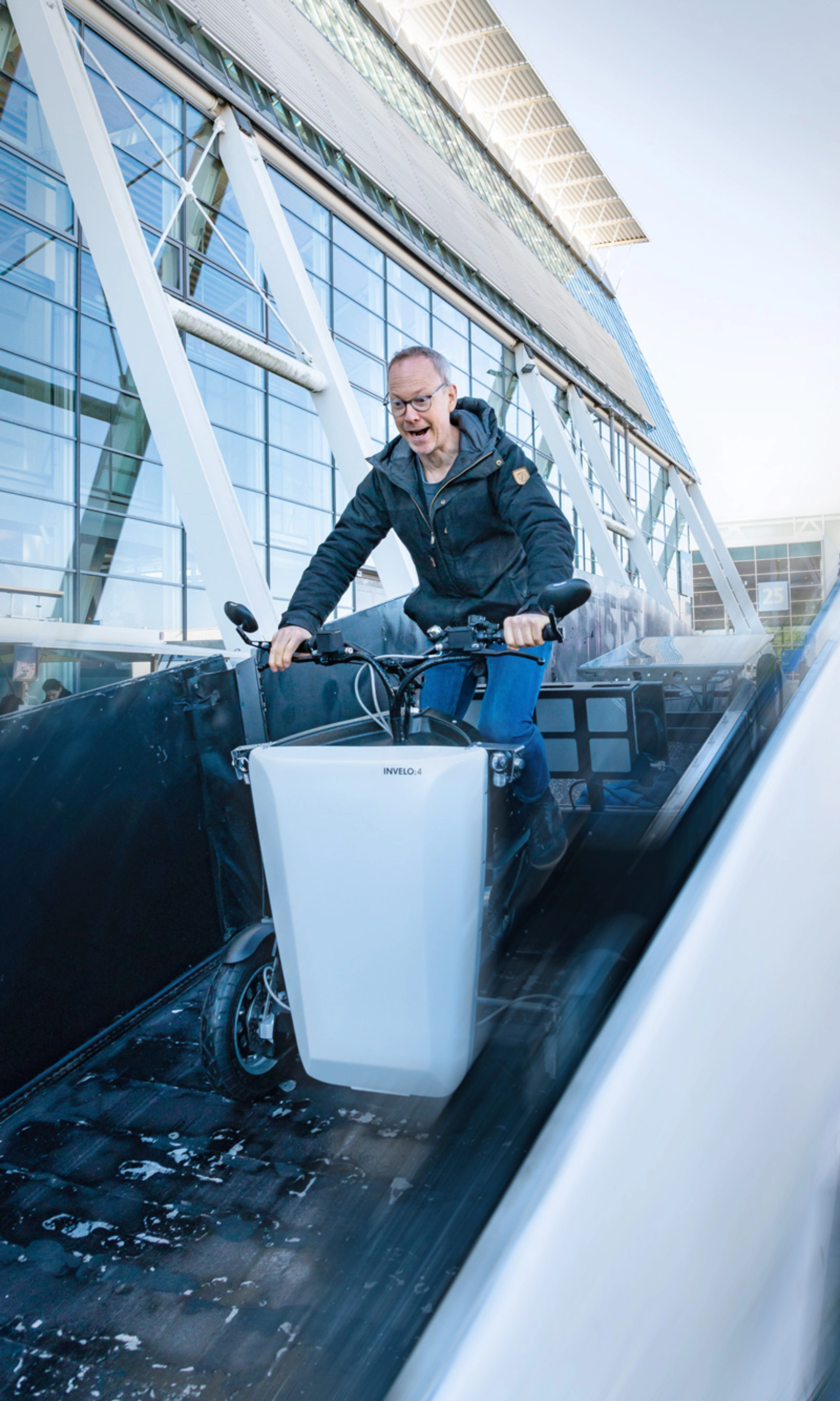 A person rides a cargo bike outside a hall with glass panels at the IAA Transportation.