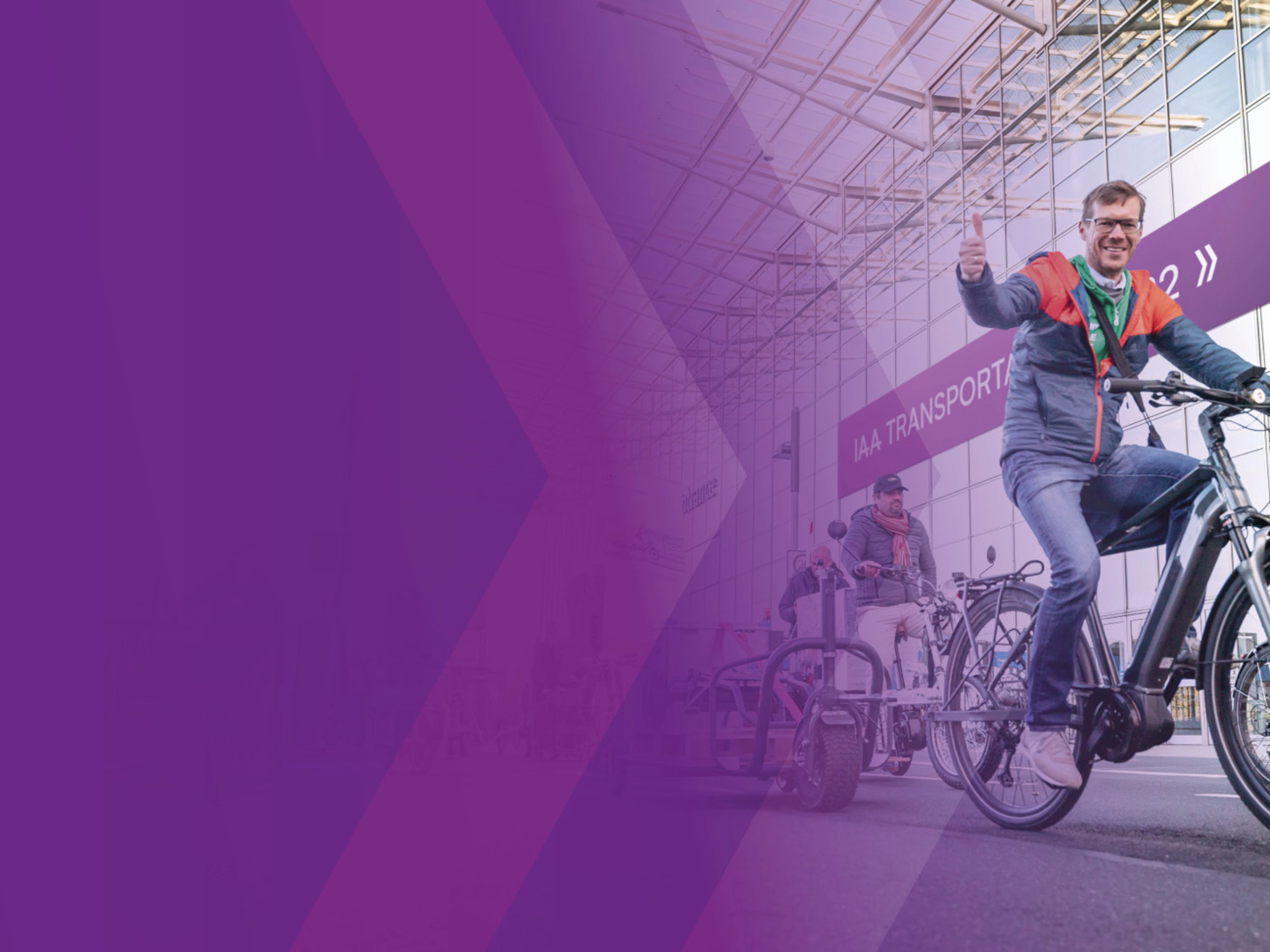 Man riding an e-bike and giving a thumbs up at a trade fair entrance.