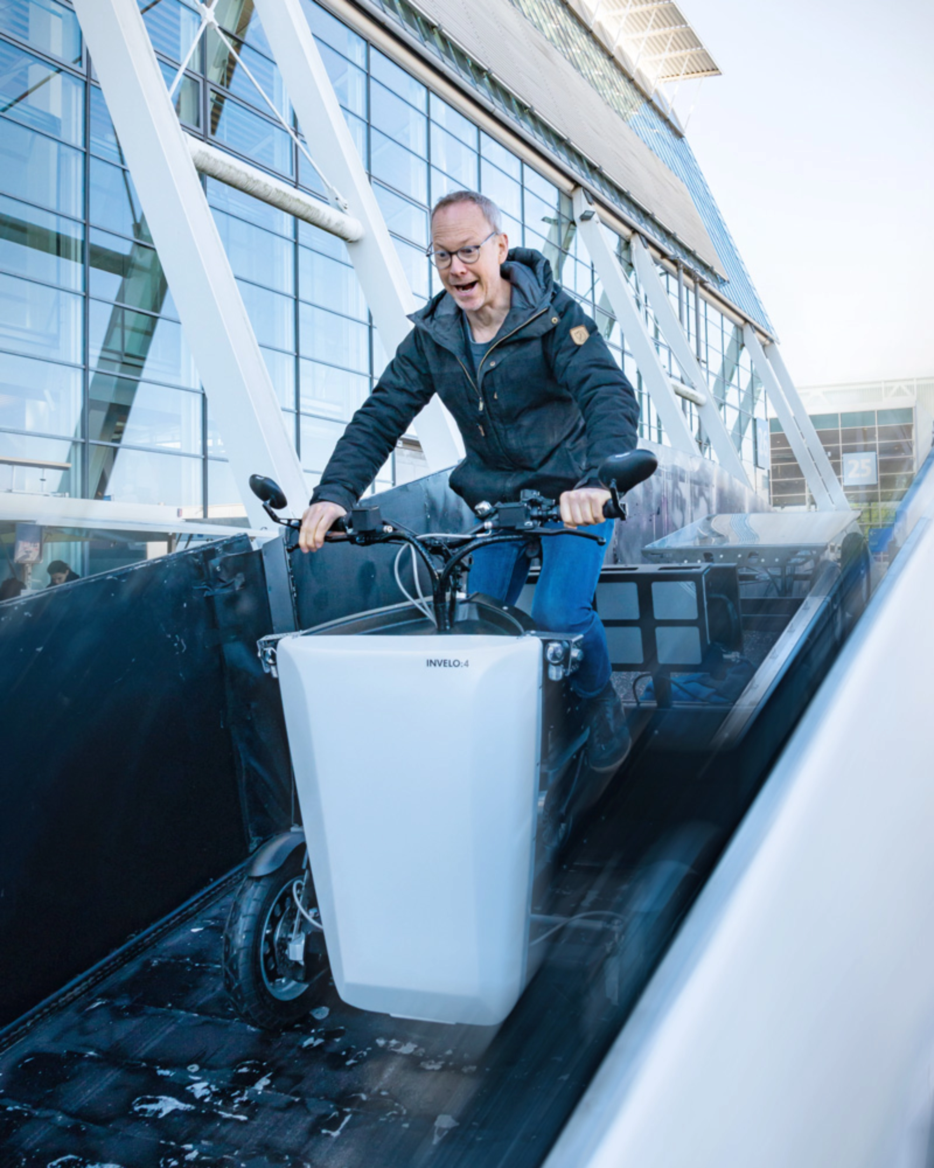 A person rides a cargo bike outside a hall with glass panels at the IAA Transportation.