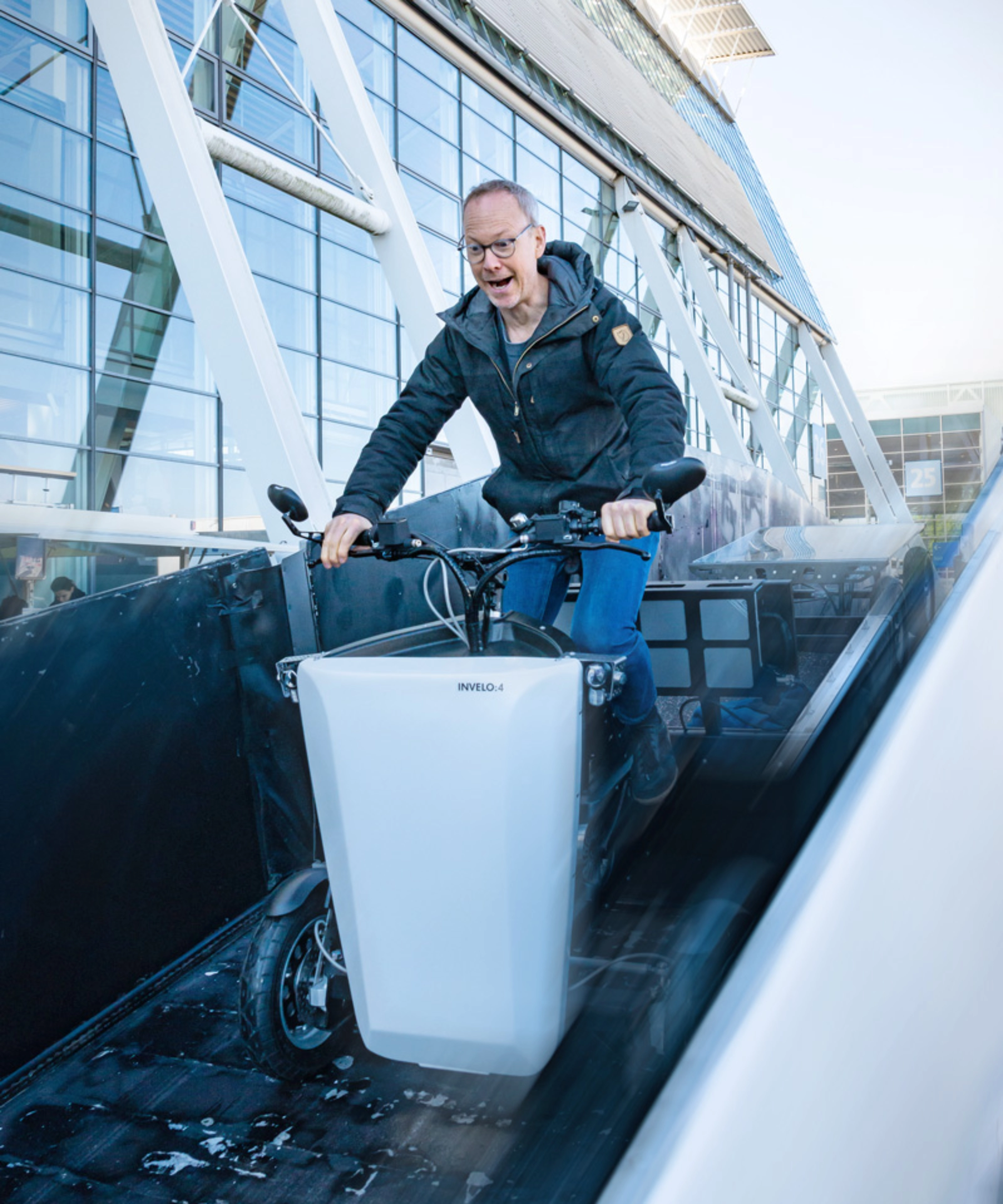 A person rides a cargo bike outside a hall with glass panels at the IAA Transportation.