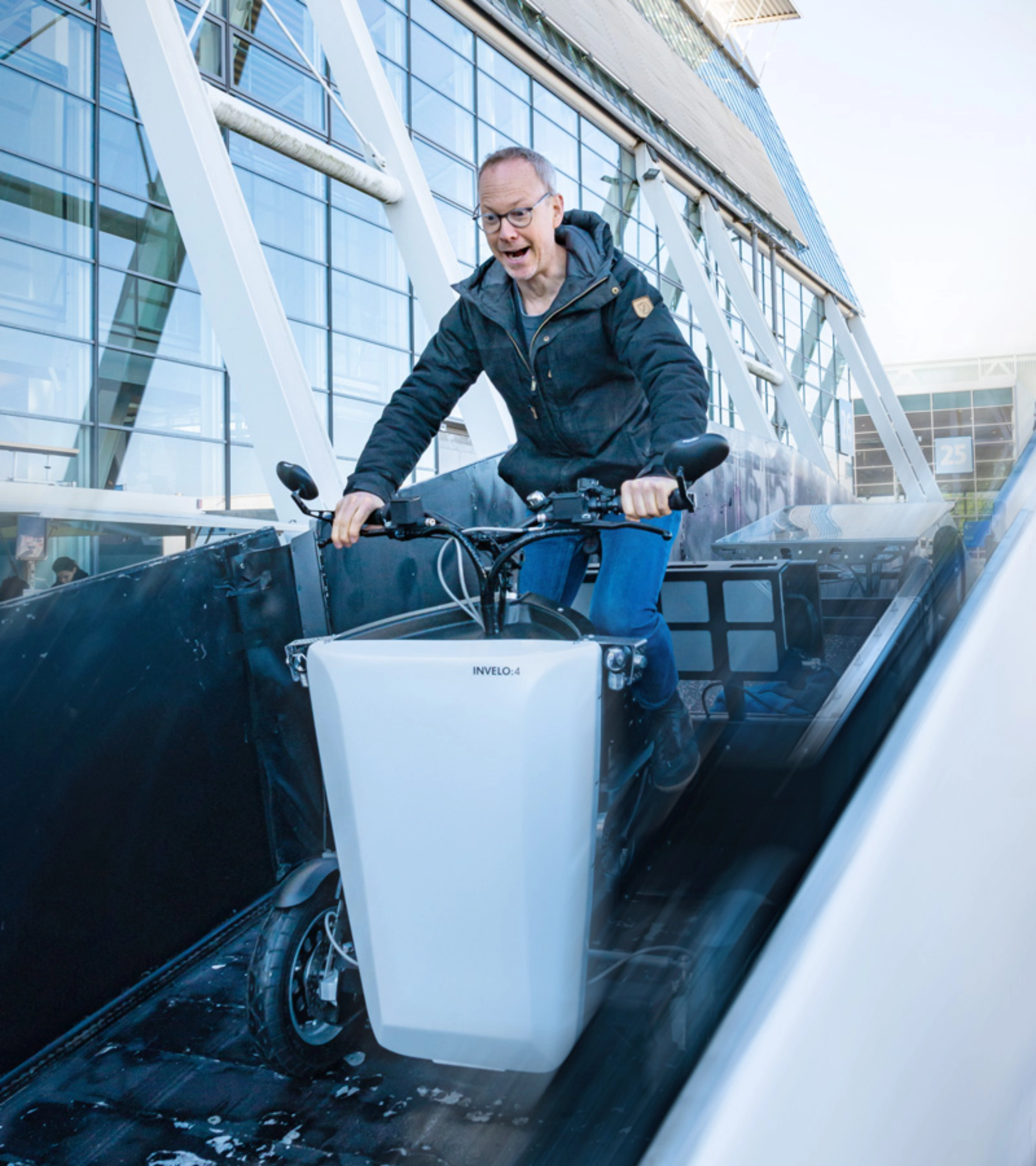 A person rides a cargo bike outside a hall with glass panels at the IAA Transportation.