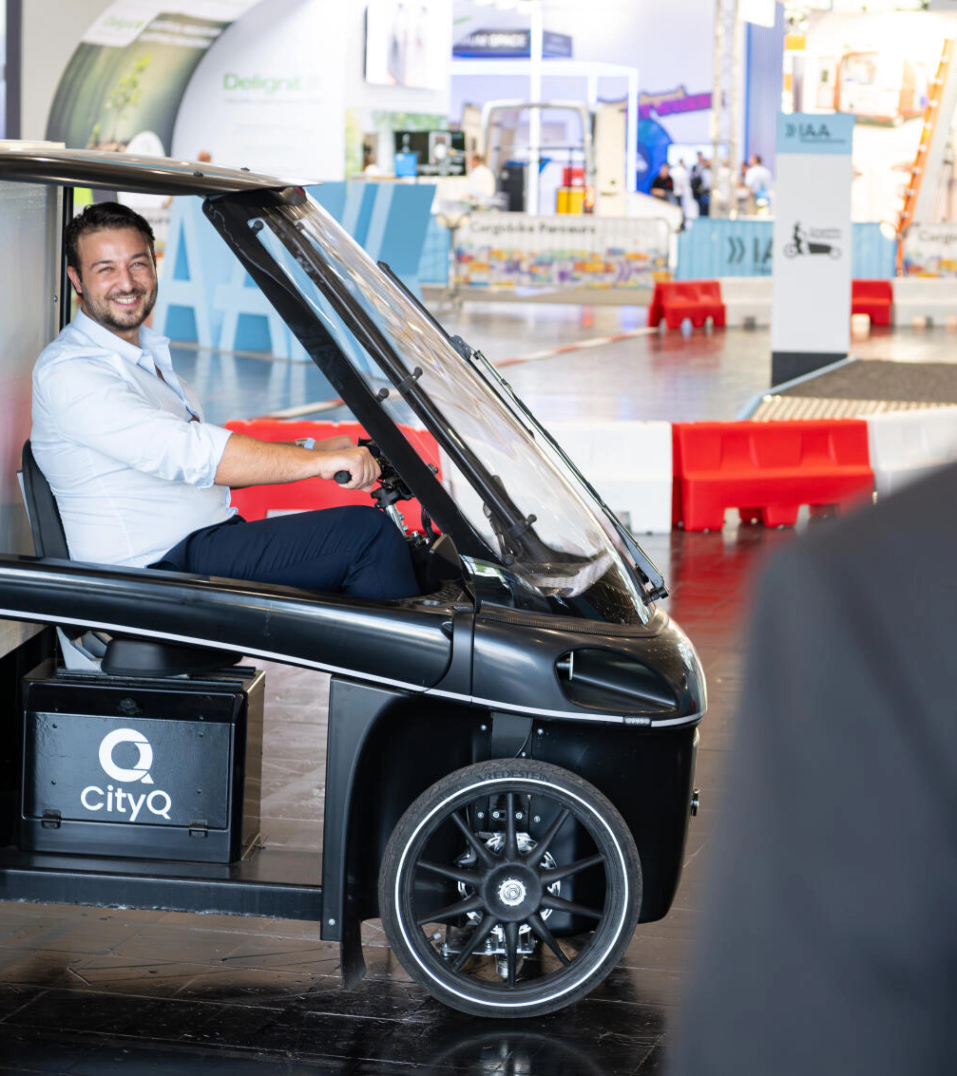Man sitting in a CityQ cargo bike inside an exhibition hall.