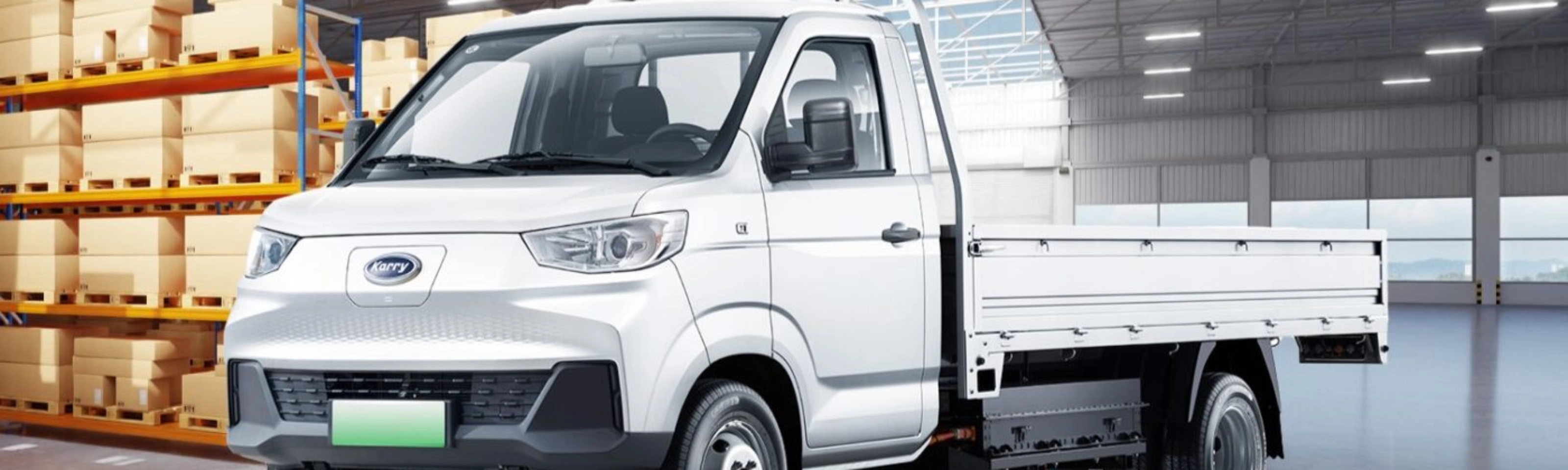 A white Karry electric flatbed truck is parked inside a warehouse near stacked boxes.
