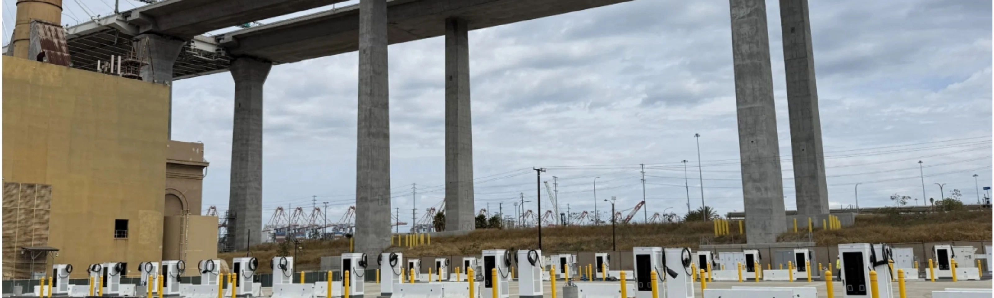 Mehrere E-Ladestationen auf einem Parkplatz unter einer Autobahnbrücke.