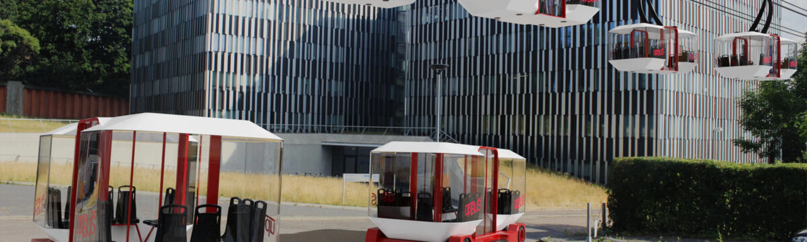 Moderne Seilbahnen und Bodenfahrzeuge des upBUS-Systems stehen vor Bürogebäuden.