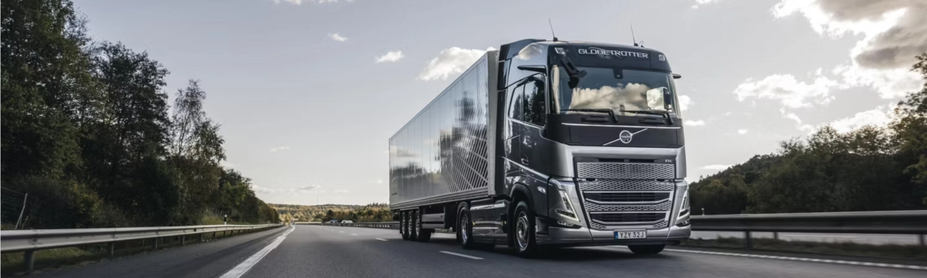 Ein moderner Volvo-Lkw fährt auf einer von Bäumen gesäumten Autobahn unter leicht bewölktem Himmel.