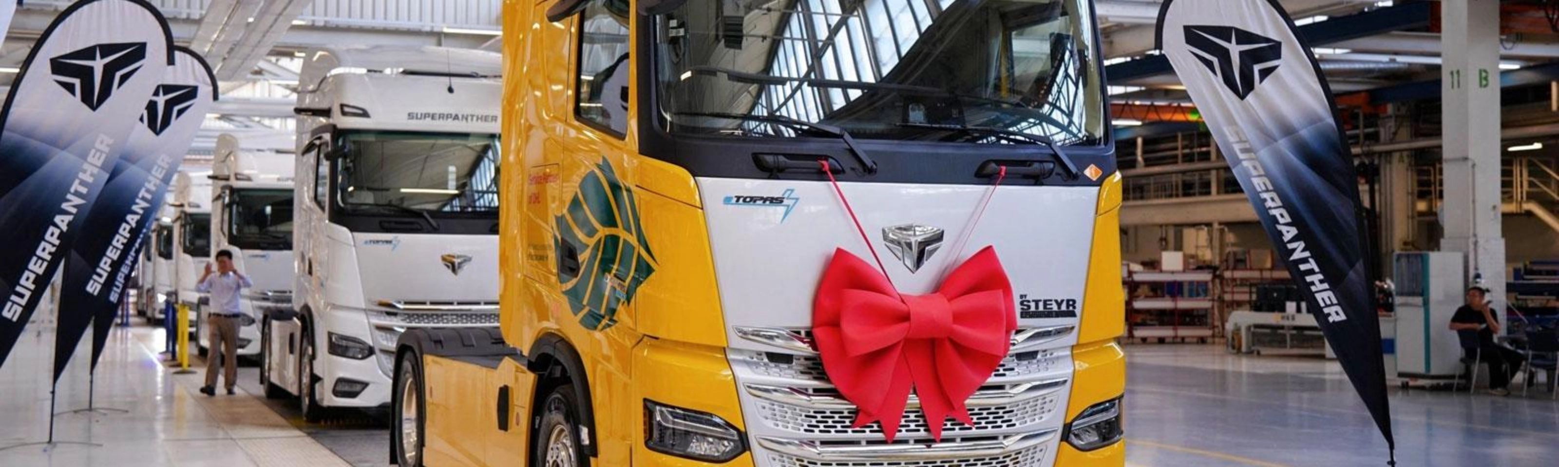 DHL electric truck with a red gift bow displayed inside a production hall.