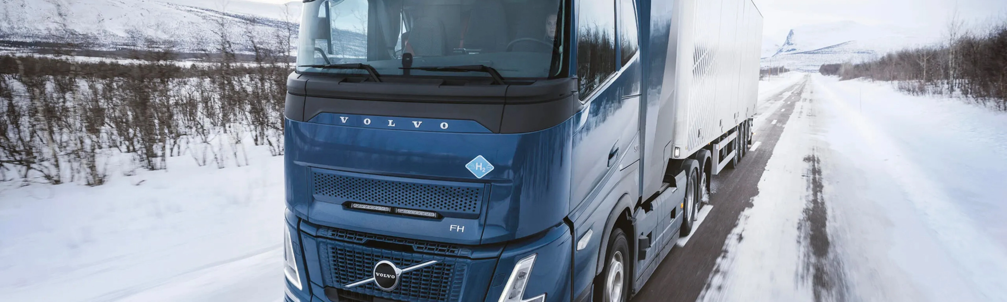 Wasserstoffbetriebener Volvo-Lkw fährt auf verschneiter Straße durch Winterlandschaft.