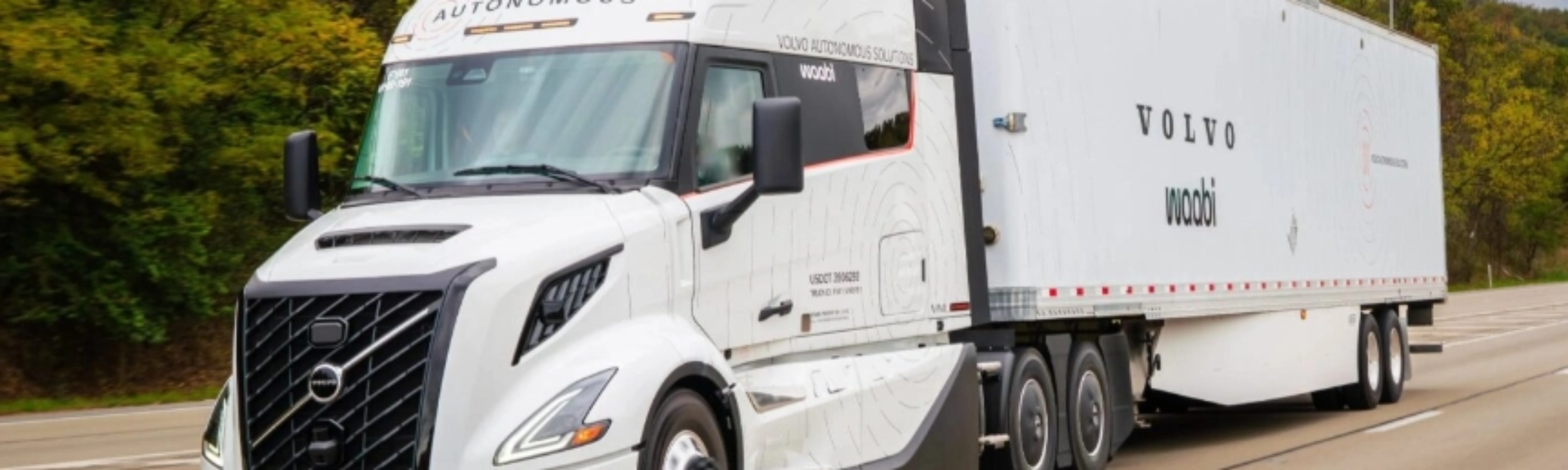 Ein weißer autonomer Volvo-Lkw mit Waabi-Logo fährt auf einer Autobahn an Bäumen vorbei.