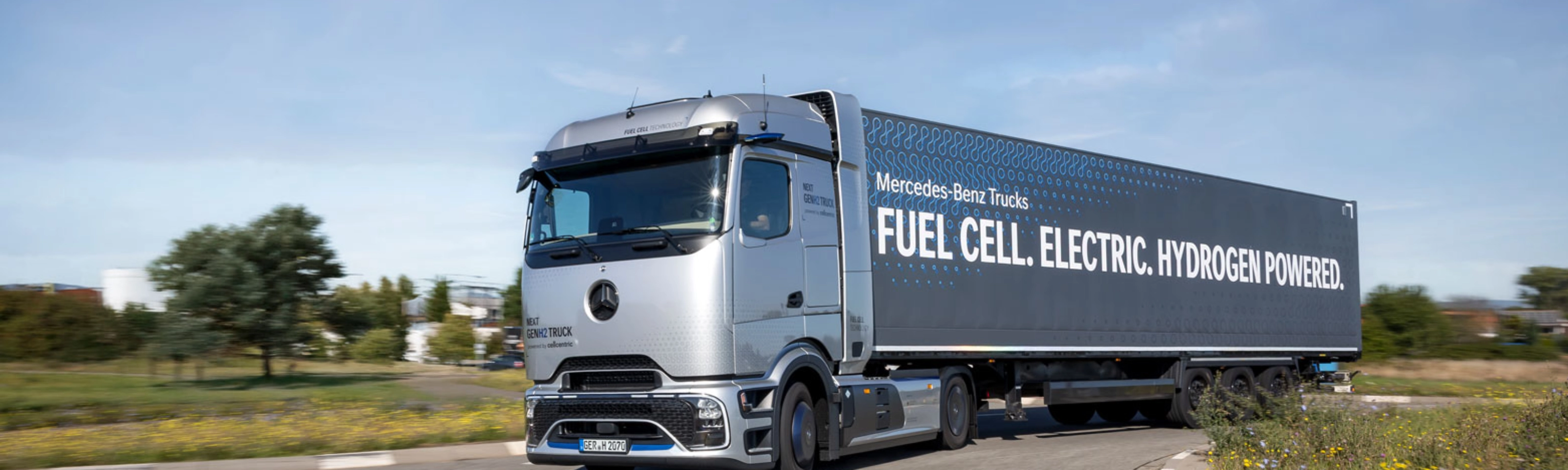 Wasserstoffbetriebener Mercedes-Lkw fährt auf einer kurvigen Straße im ländlichen Gebiet.