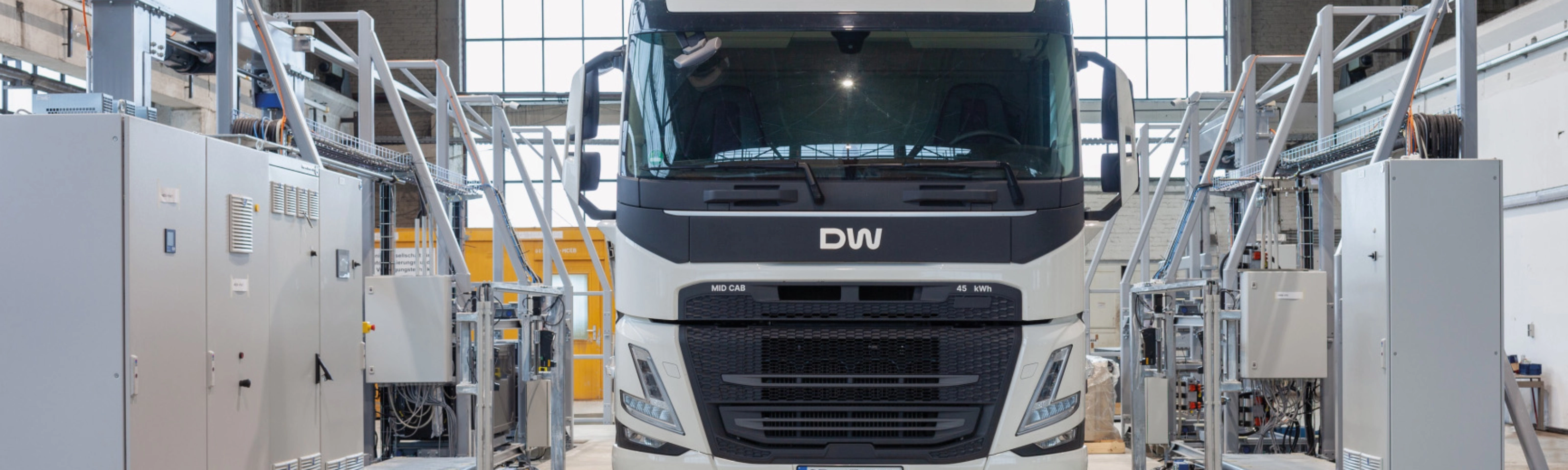 Electric truck in a test hall, surrounded by technical equipment and control cabinets.