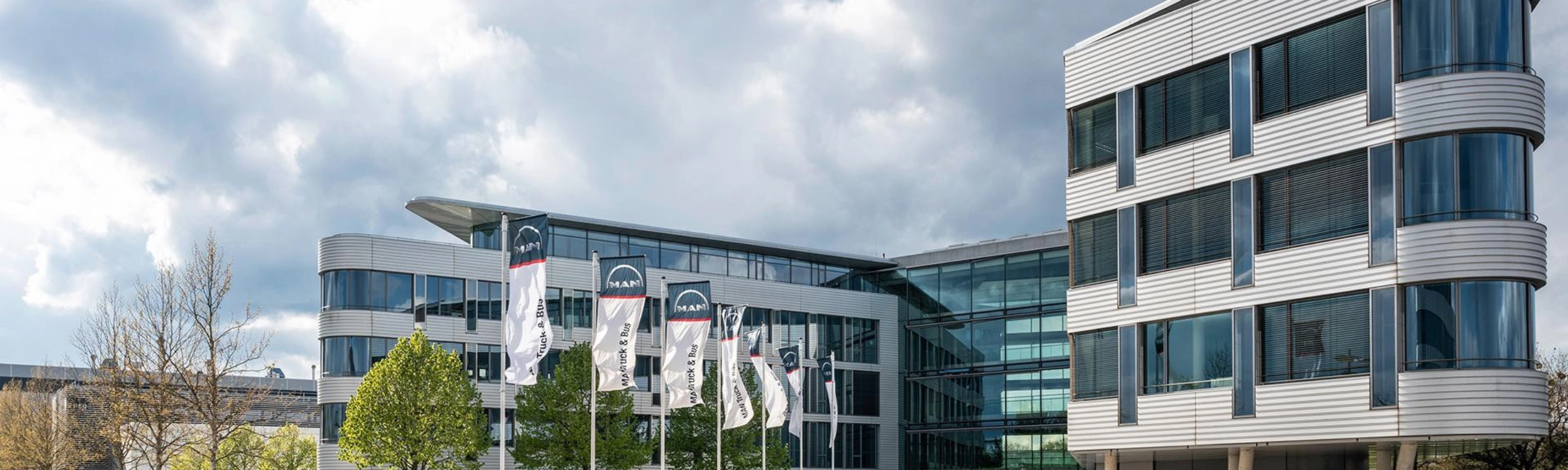 Modern office building with glass facade and MAN Truck & Bus flags in front.