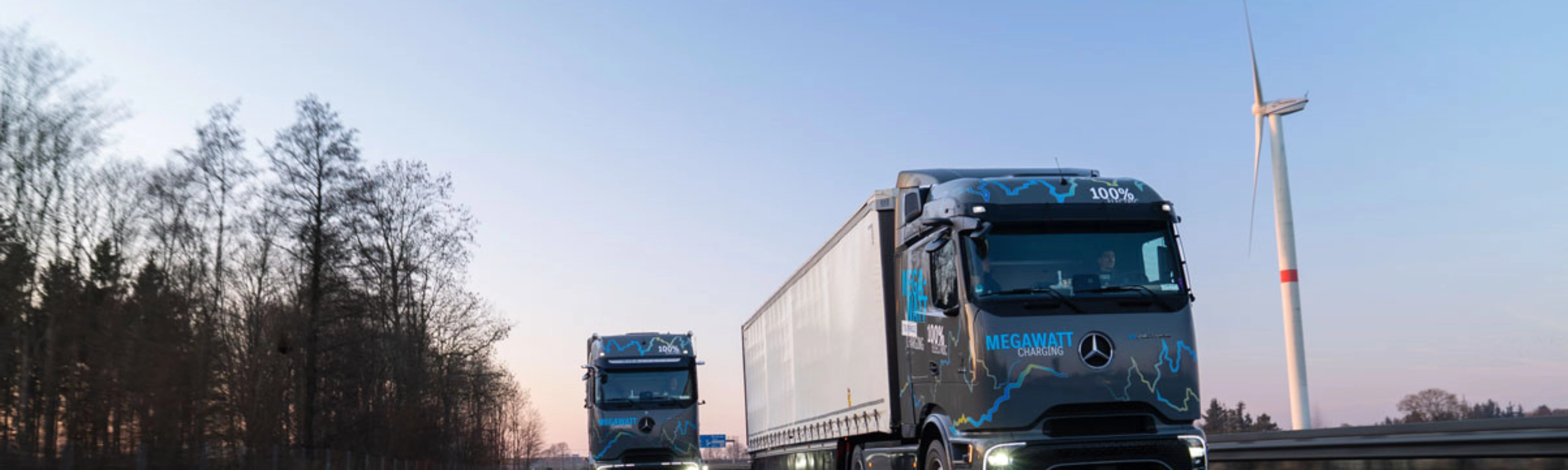 Zwei elektrische Mercedes-Benz-Lkw mit „Megawatt Charging“-Aufschrift fahren bei Dämmerung auf der Autobahn.