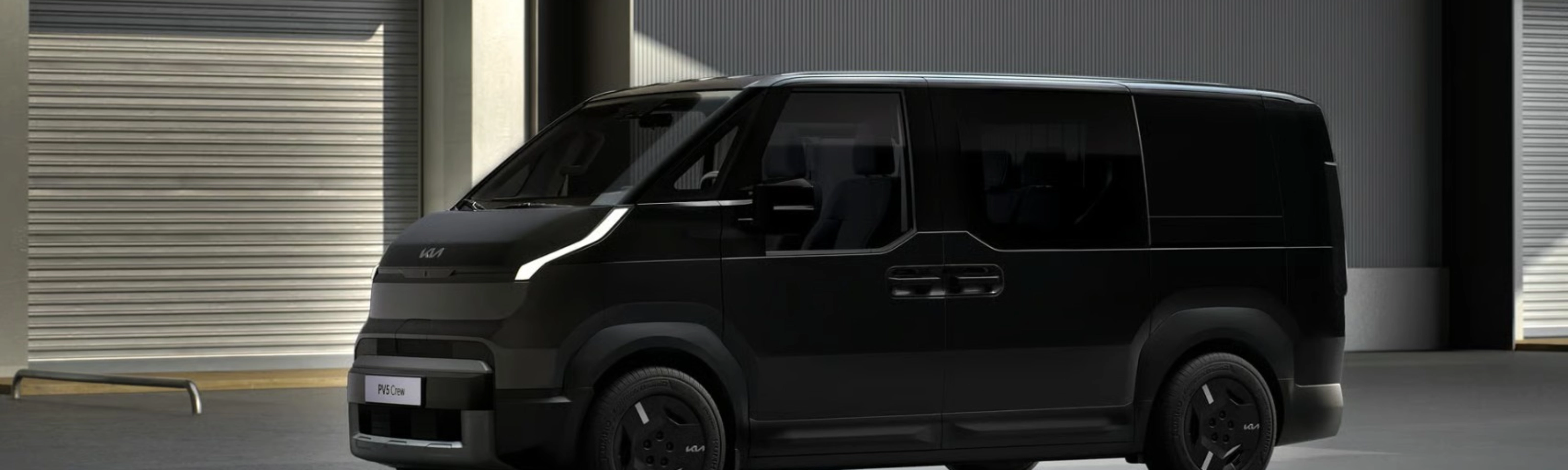 Schwarzer Kia-Van steht vor Industriegebäuden mit geschlossenen Rolltoren.