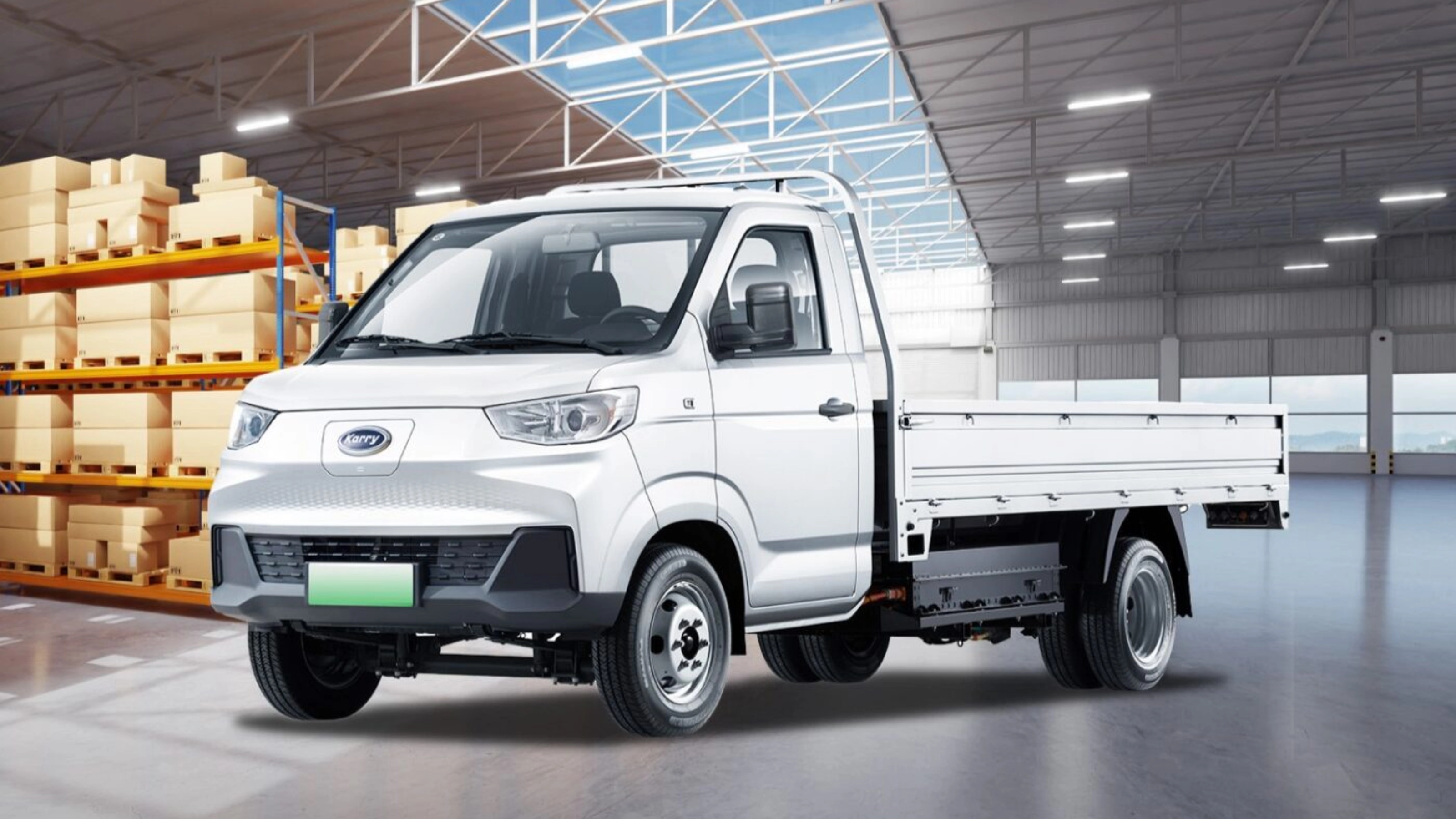 A white Karry electric flatbed truck is parked inside a warehouse near stacked boxes.