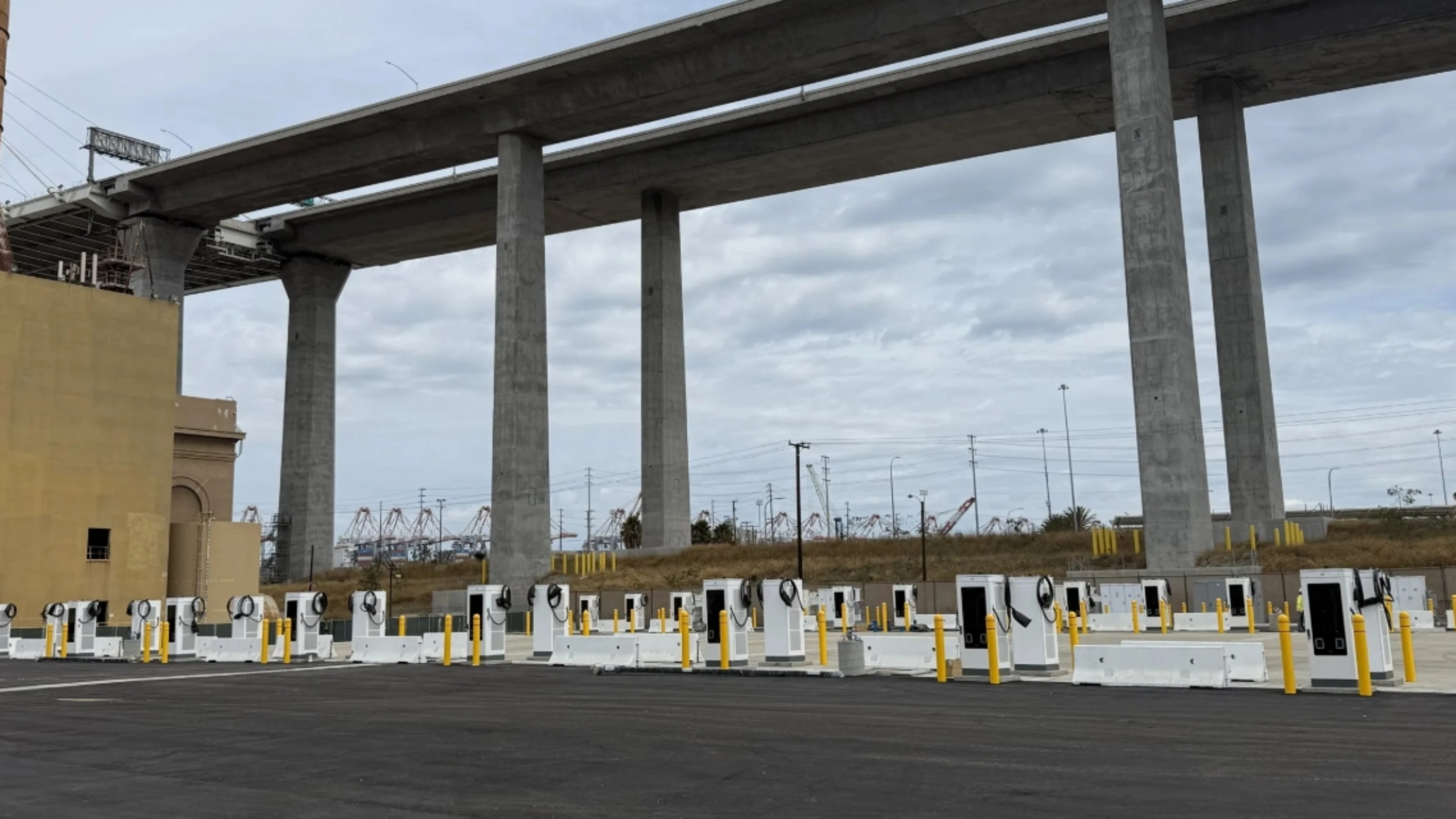 Mehrere E-Ladestationen auf einem Parkplatz unter einer Autobahnbrücke.