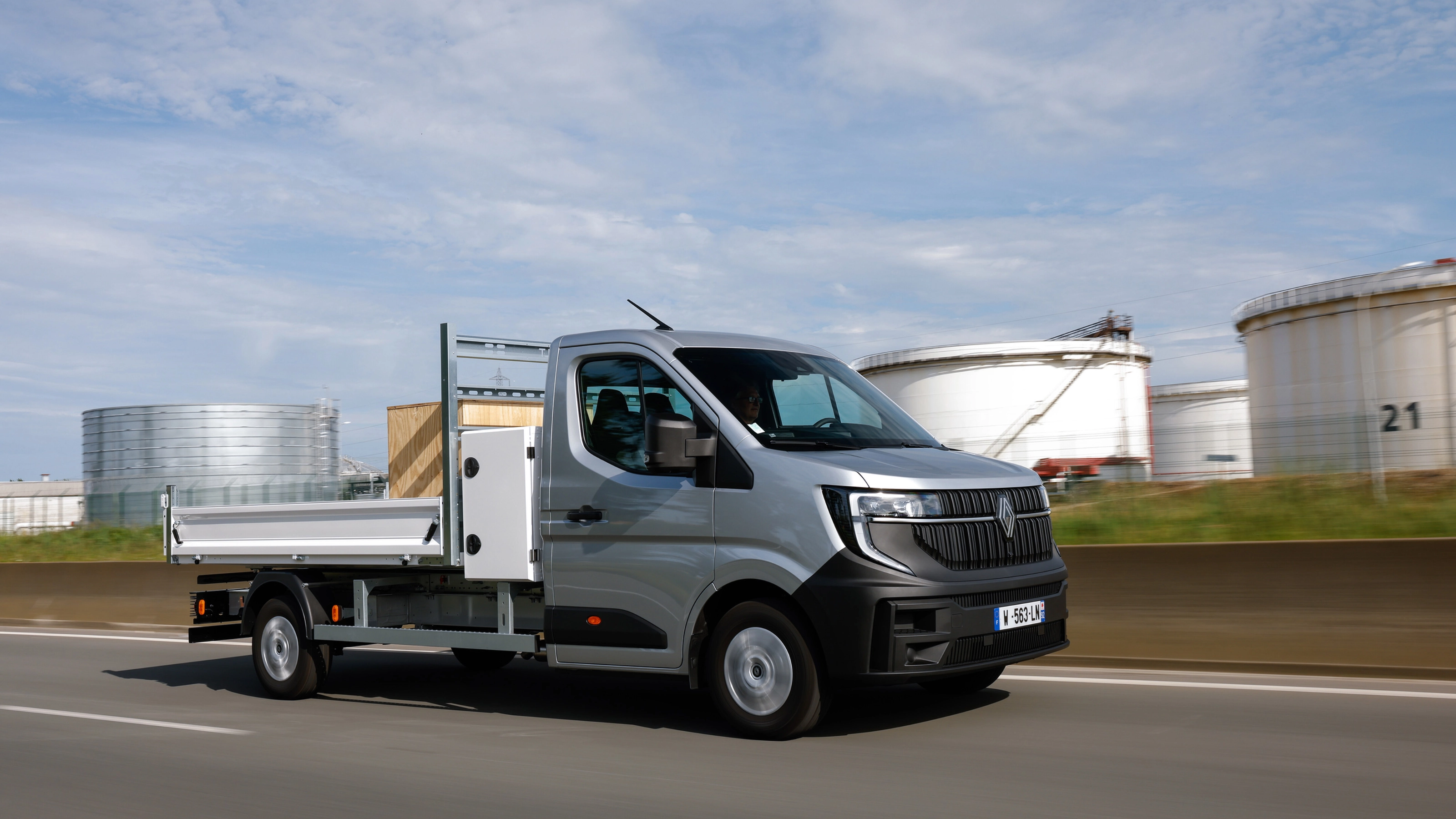 Grey Renault flatbed truck driving on a road in an industrial area.