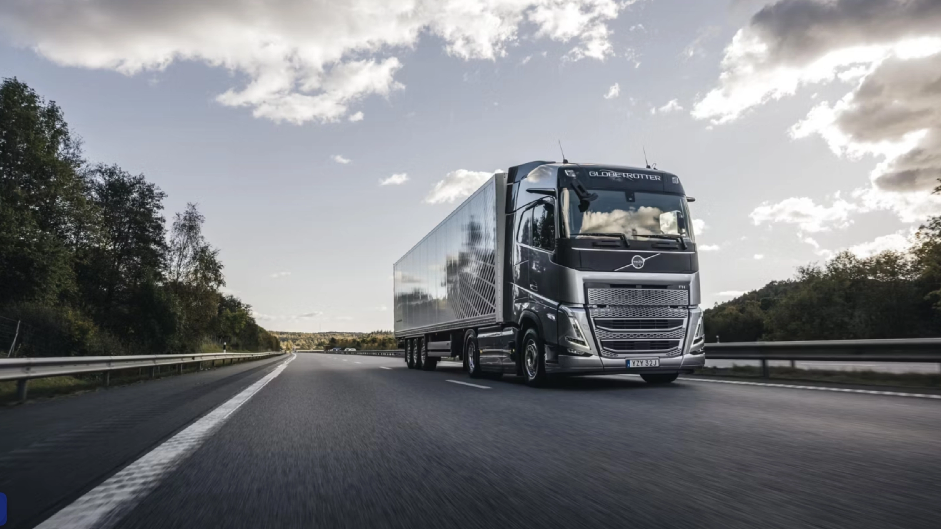Ein moderner Volvo-Lkw fährt auf einer von Bäumen gesäumten Autobahn unter leicht bewölktem Himmel.