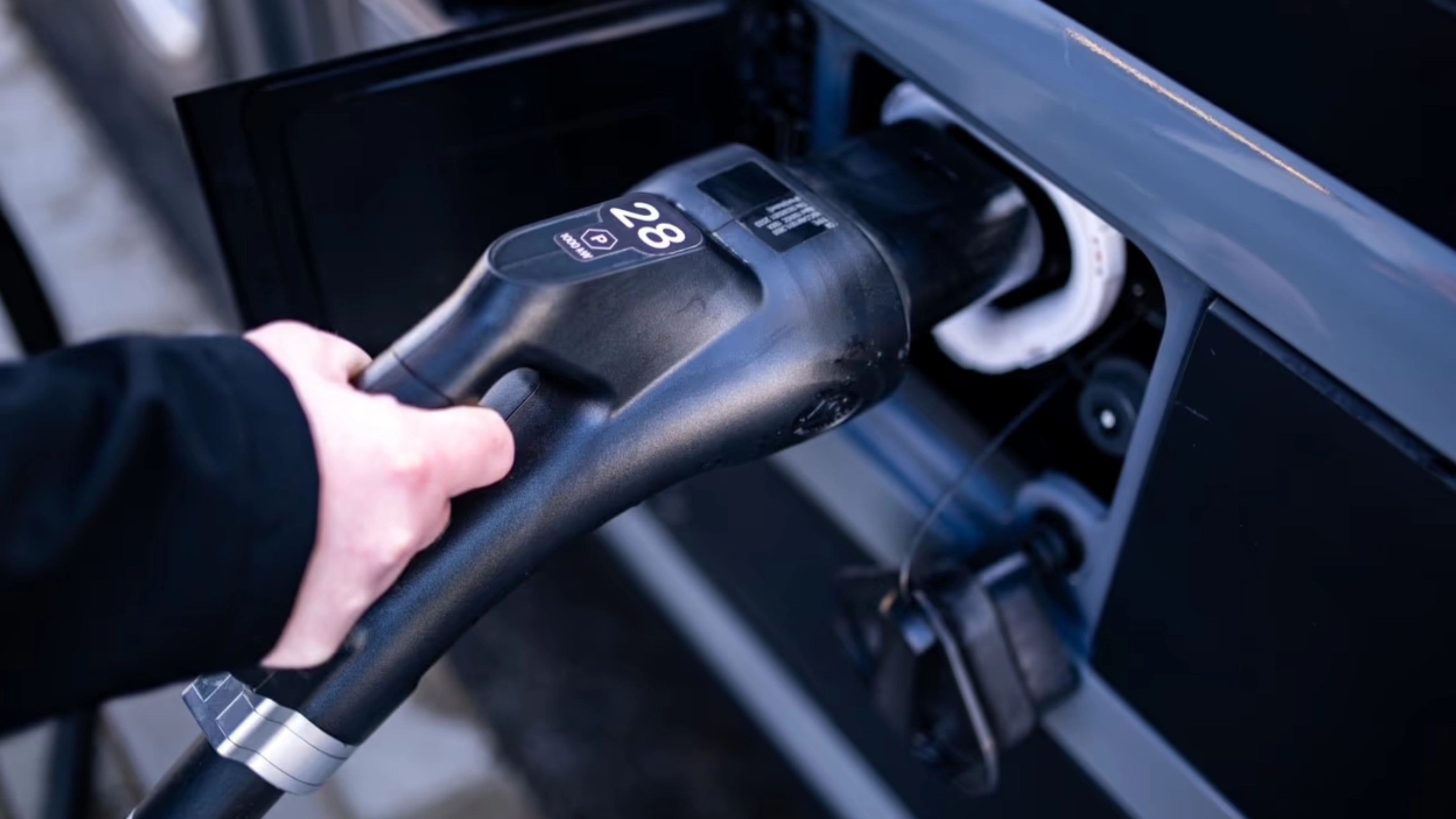 A person plugs a charging connector into the charging port of a vehicle.