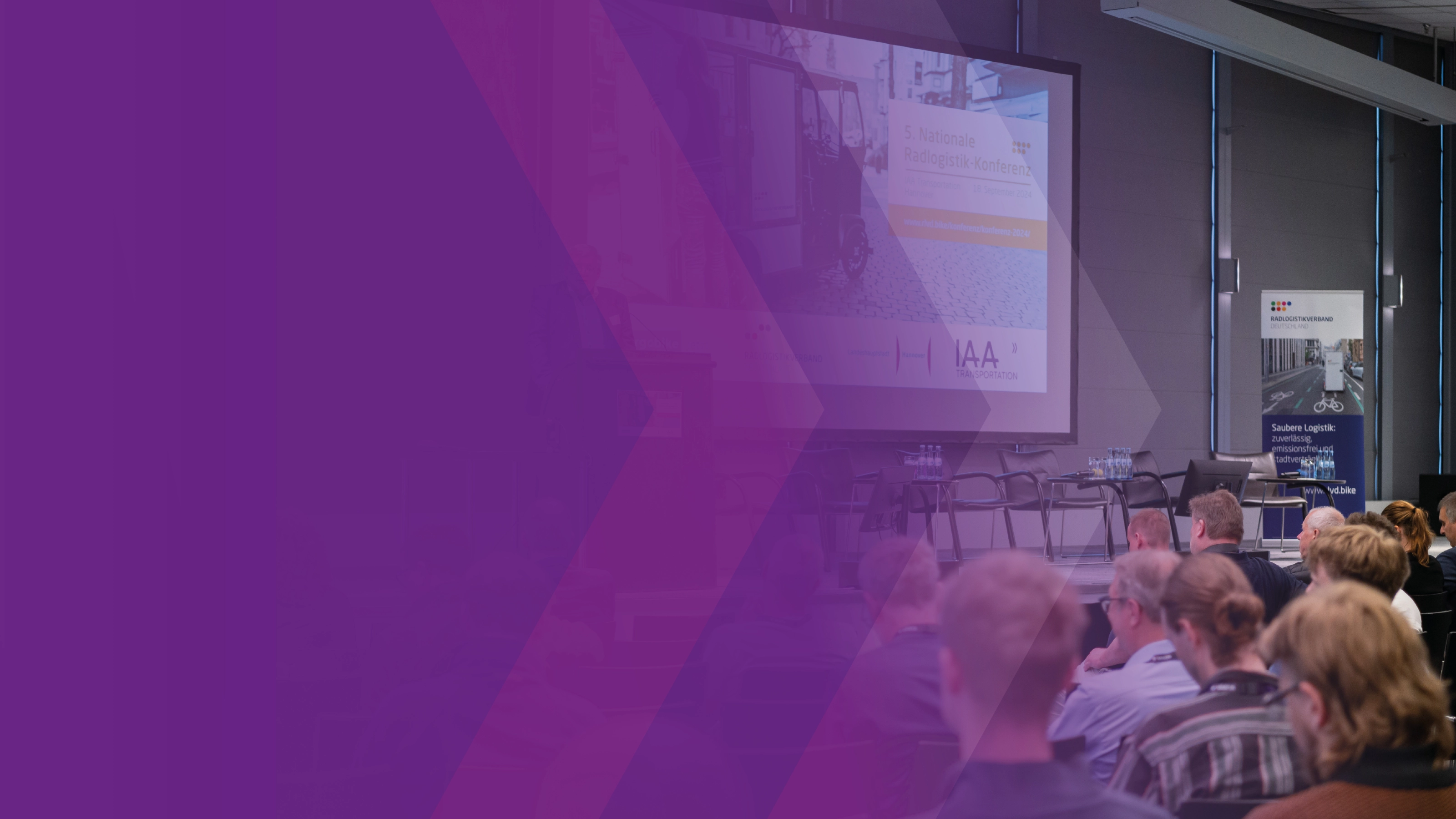 Audience seated before a stage with a presentation screen at a logistics conference.