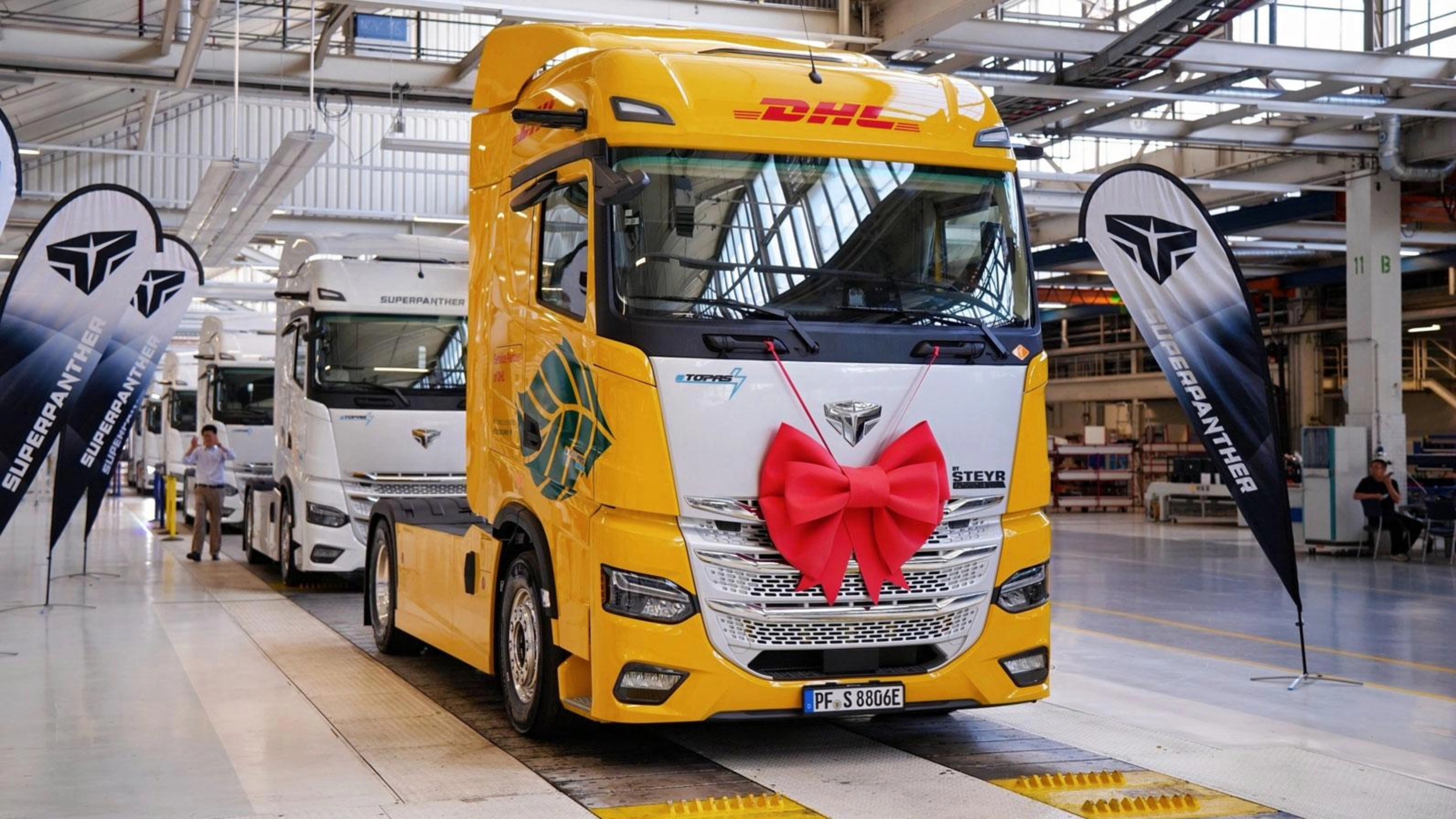 DHL electric truck with a red gift bow displayed inside a production hall.