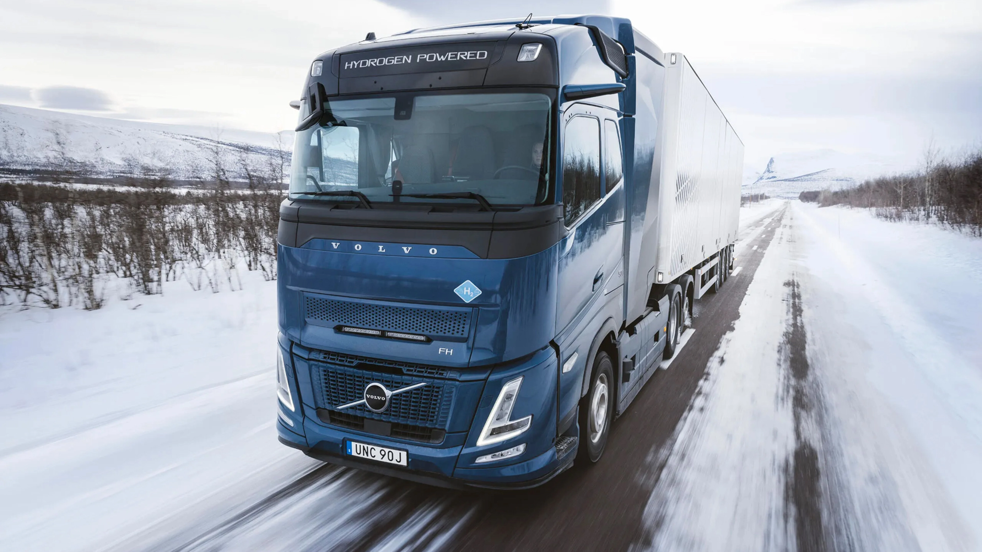 Wasserstoffbetriebener Volvo-Lkw fährt auf verschneiter Straße durch Winterlandschaft.