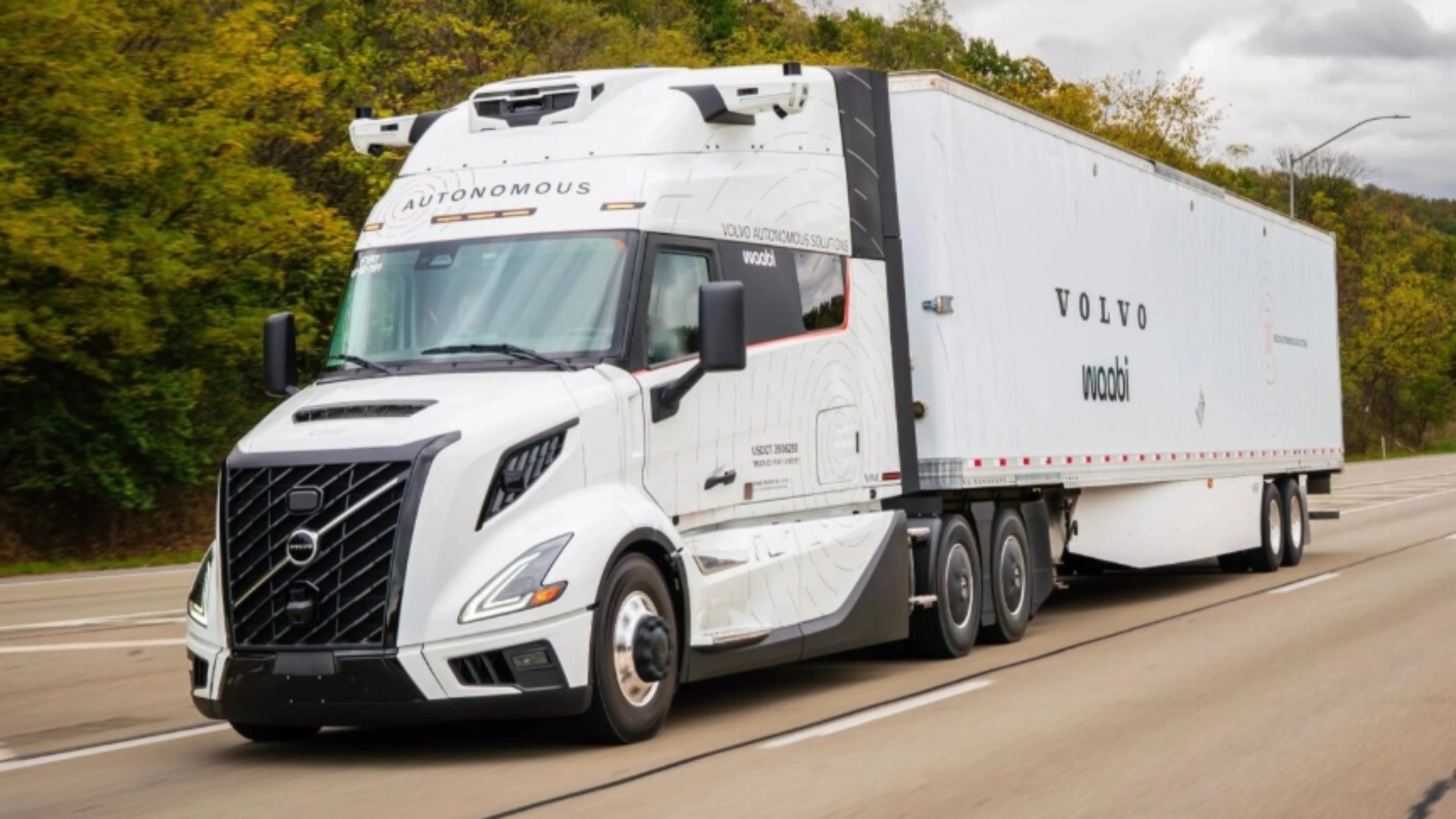 Ein weißer autonomer Volvo-Lkw mit Waabi-Logo fährt auf einer Autobahn an Bäumen vorbei.