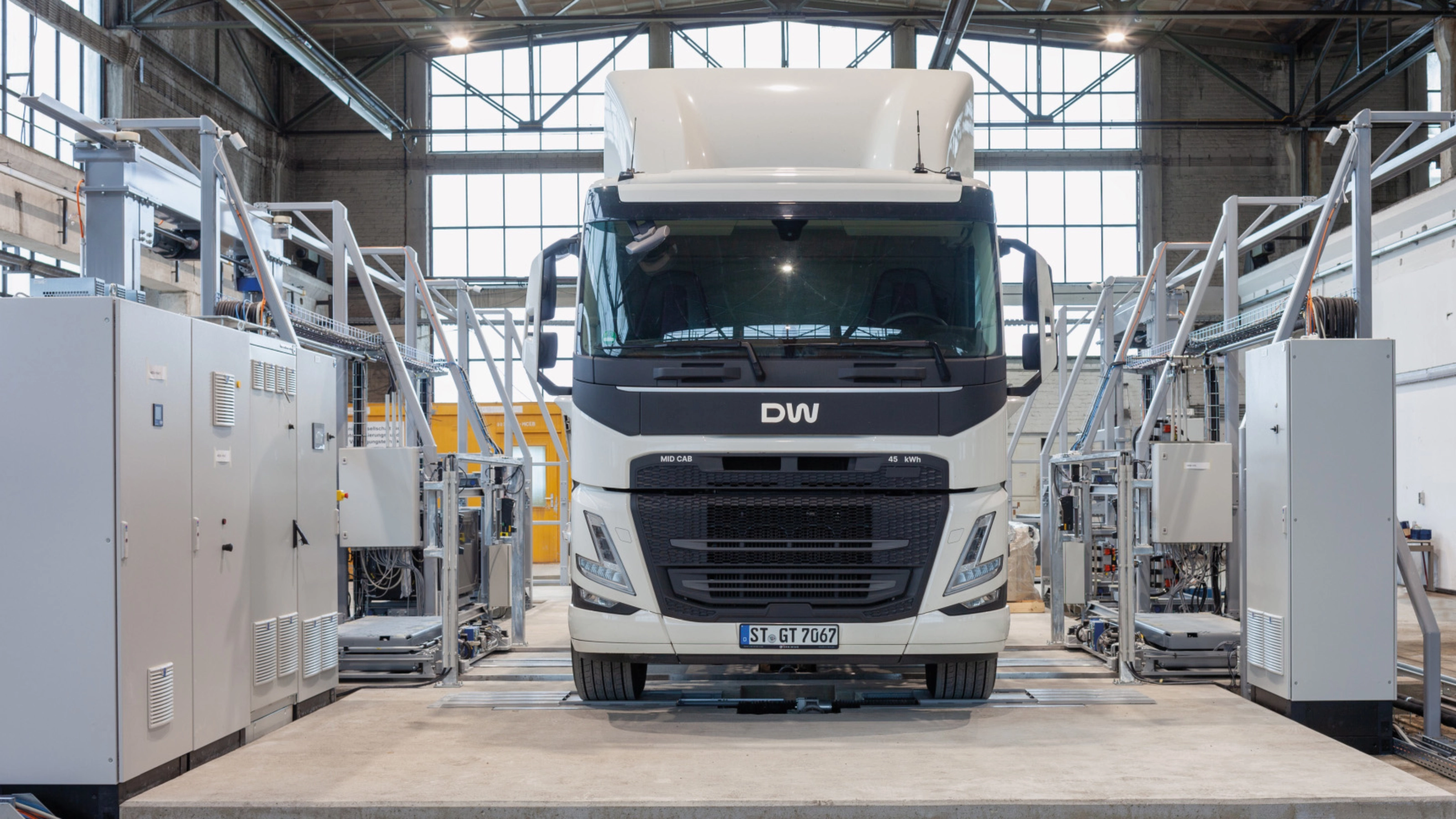 Electric truck in a test hall, surrounded by technical equipment and control cabinets.