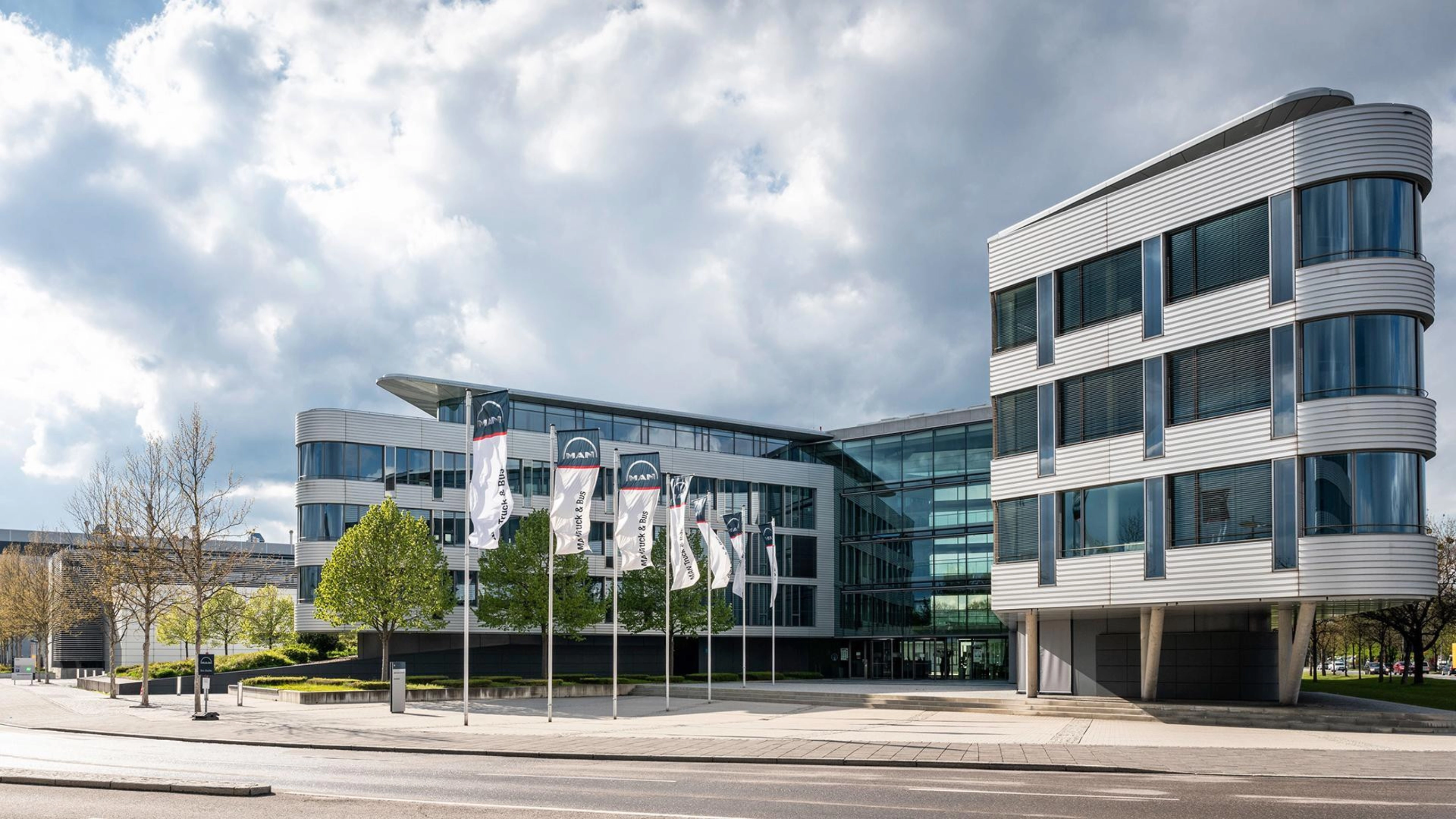 Modern office building with glass facade and MAN Truck & Bus flags in front.