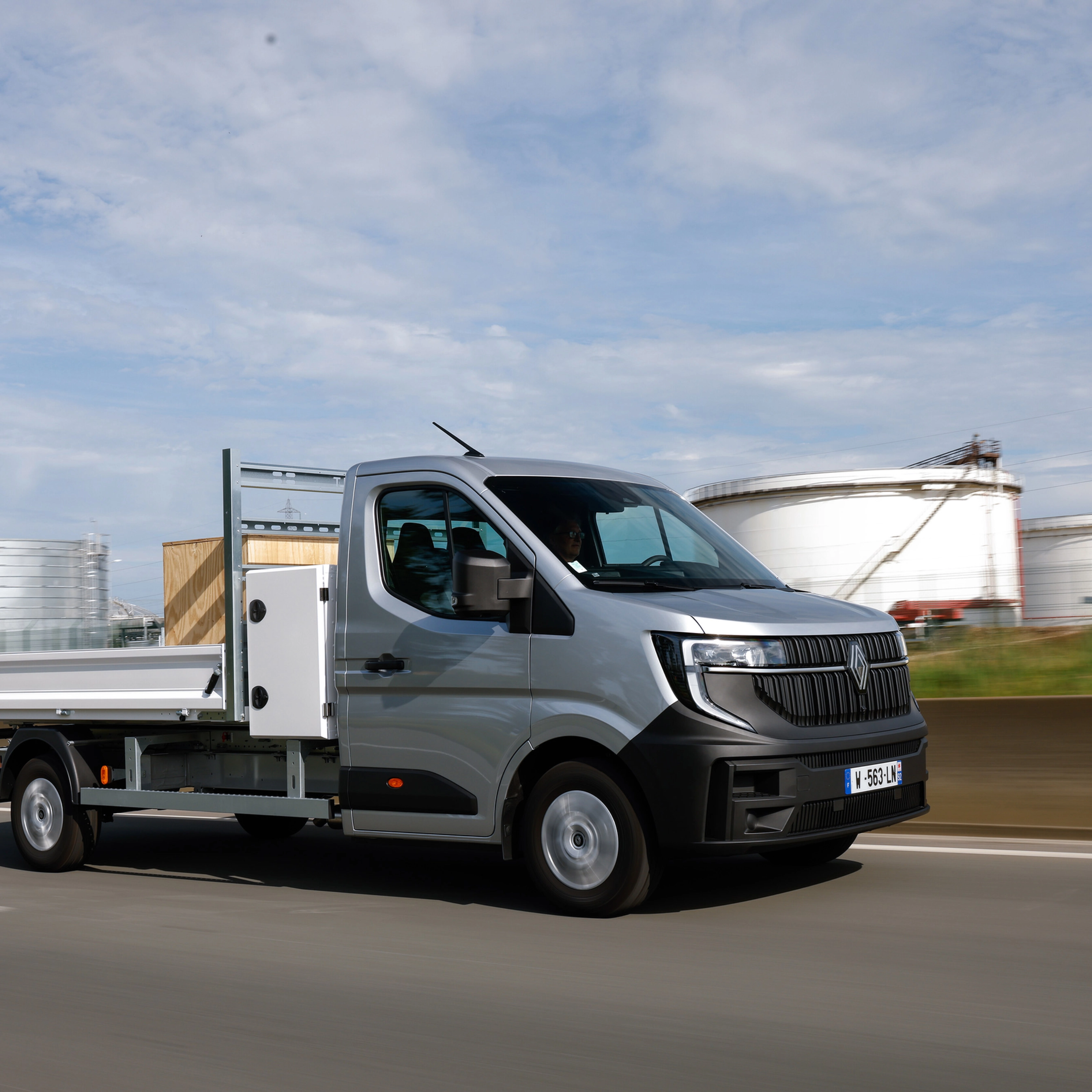 Grey Renault flatbed truck driving on a road in an industrial area.