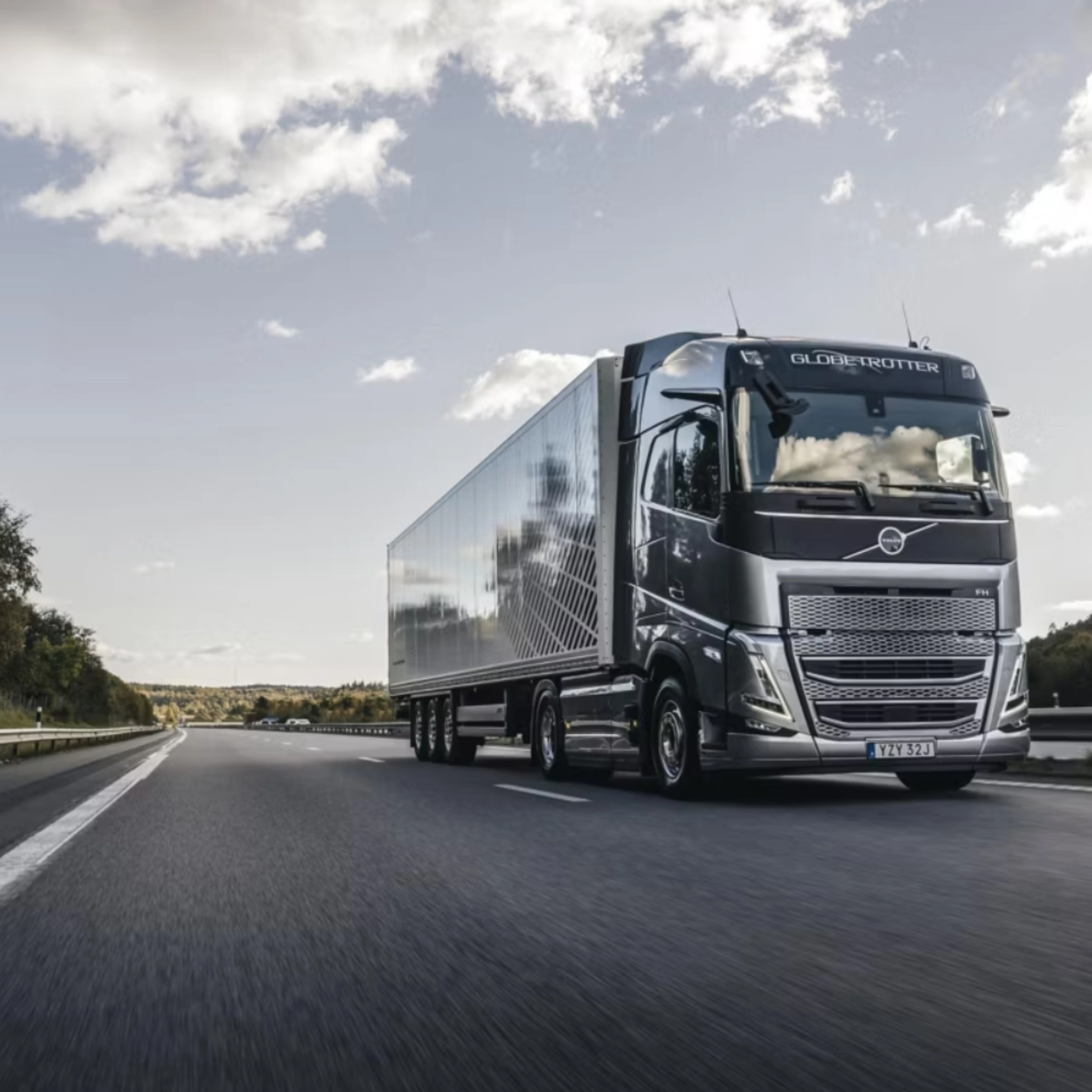 Ein moderner Volvo-Lkw fährt auf einer von Bäumen gesäumten Autobahn unter leicht bewölktem Himmel.