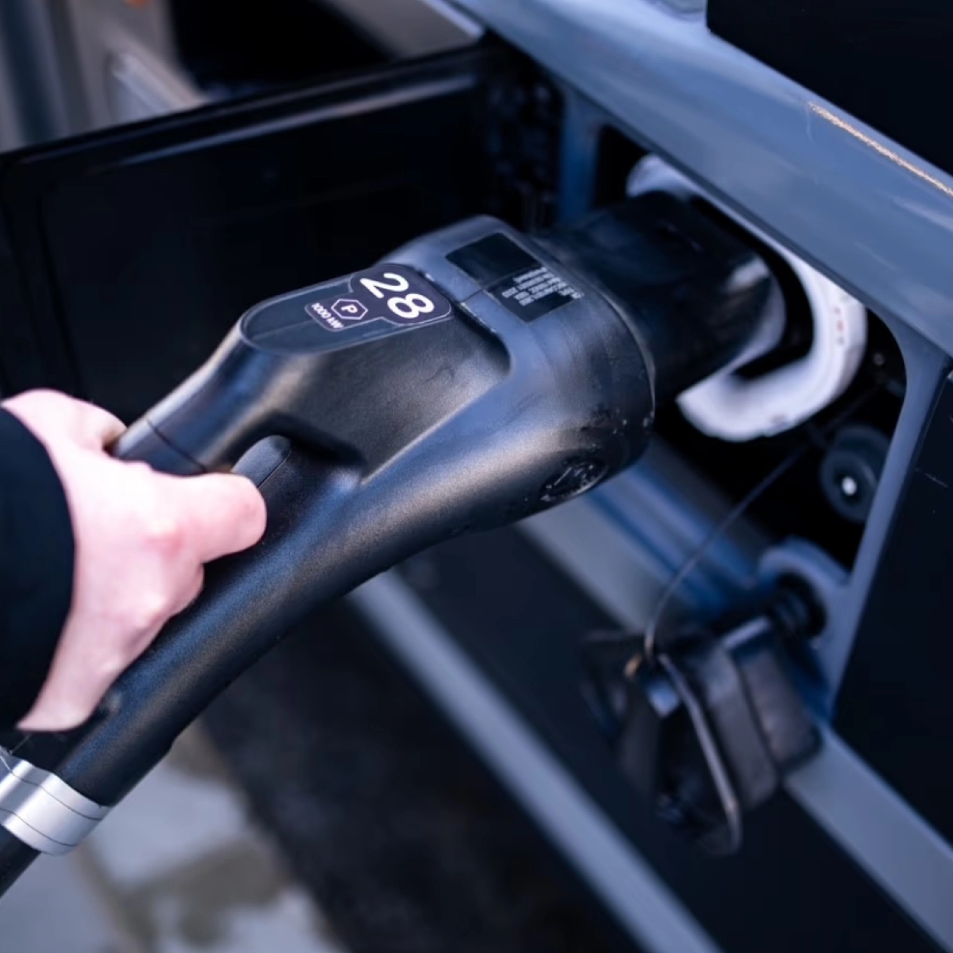 A person plugs a charging connector into the charging port of a vehicle.