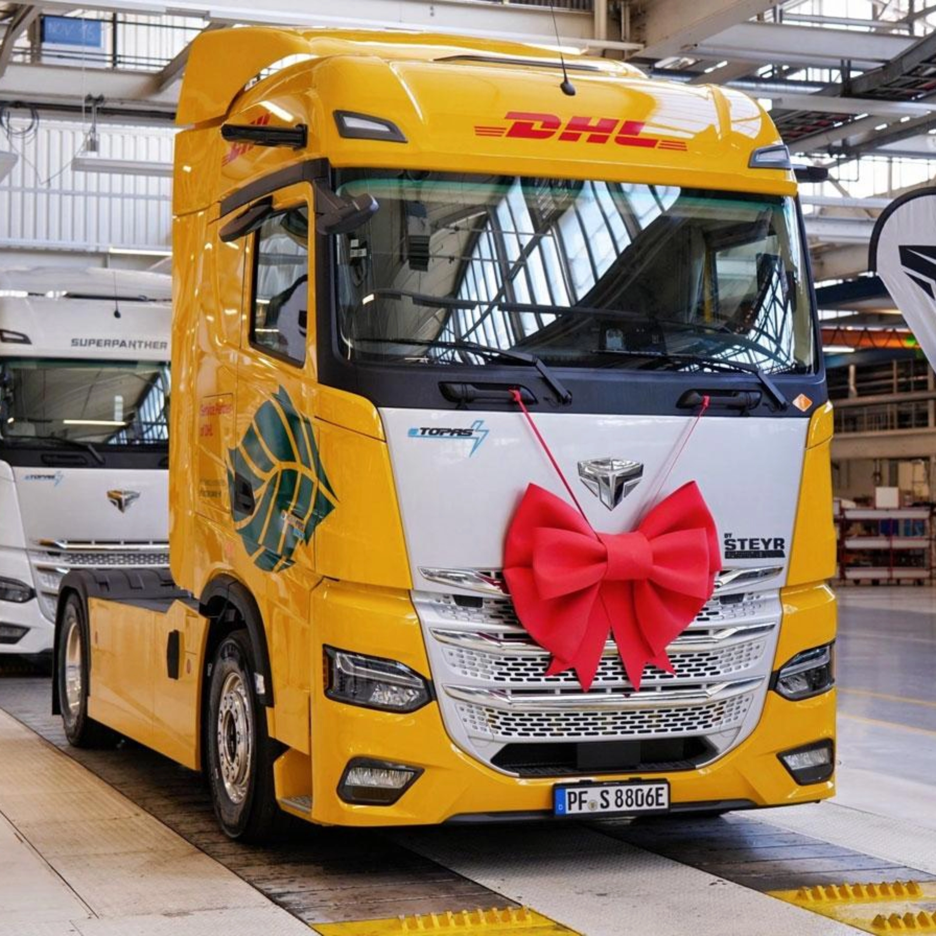 DHL electric truck with a red gift bow displayed inside a production hall.
