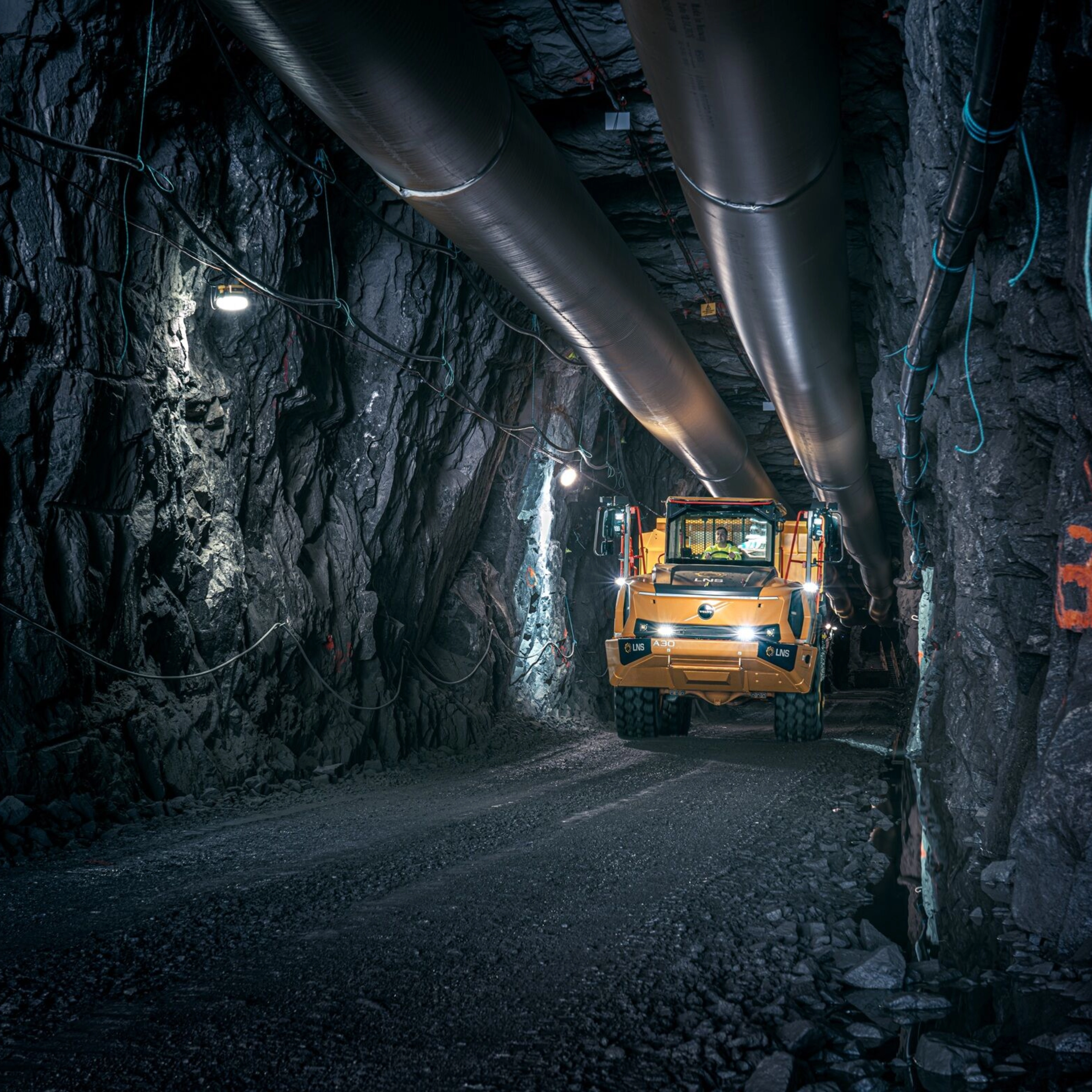 Orange Volvo truck driving through an underground mining tunnel.