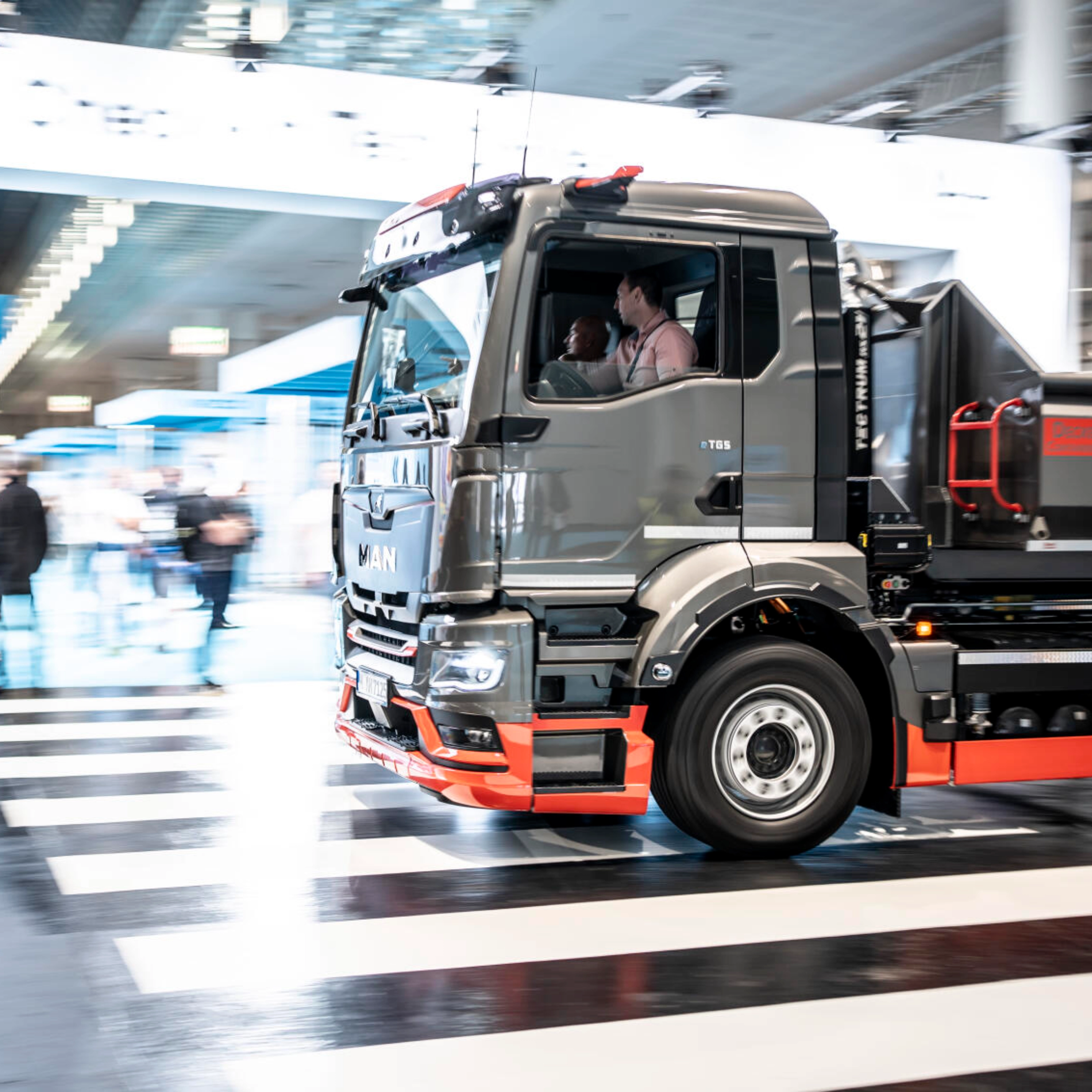 Ein MAN-Lkw fährt mit Bewegungsunschärfe durch ein Testgelände in einer Halle und überquert einen Zebrastreifen.