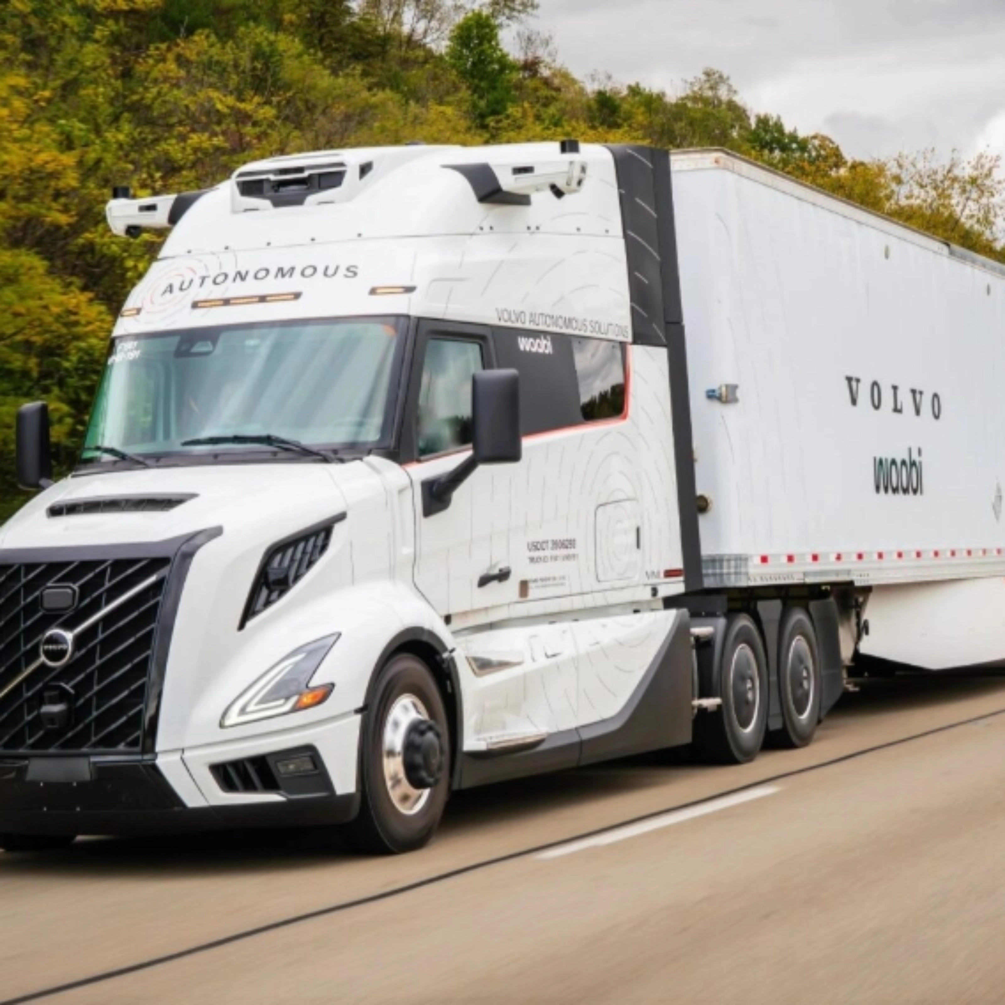 Ein weißer autonomer Volvo-Lkw mit Waabi-Logo fährt auf einer Autobahn an Bäumen vorbei.