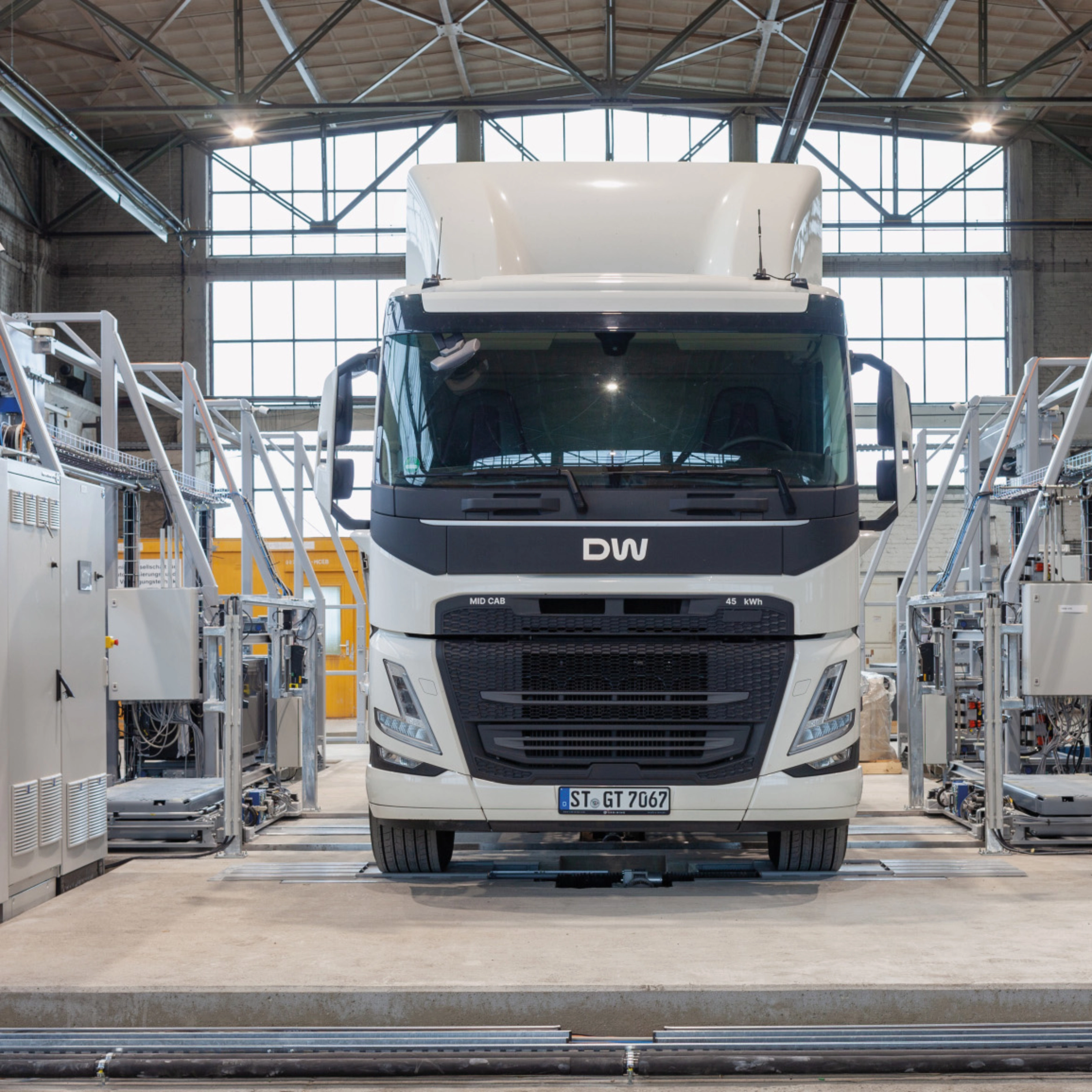 Electric truck in a test hall, surrounded by technical equipment and control cabinets.