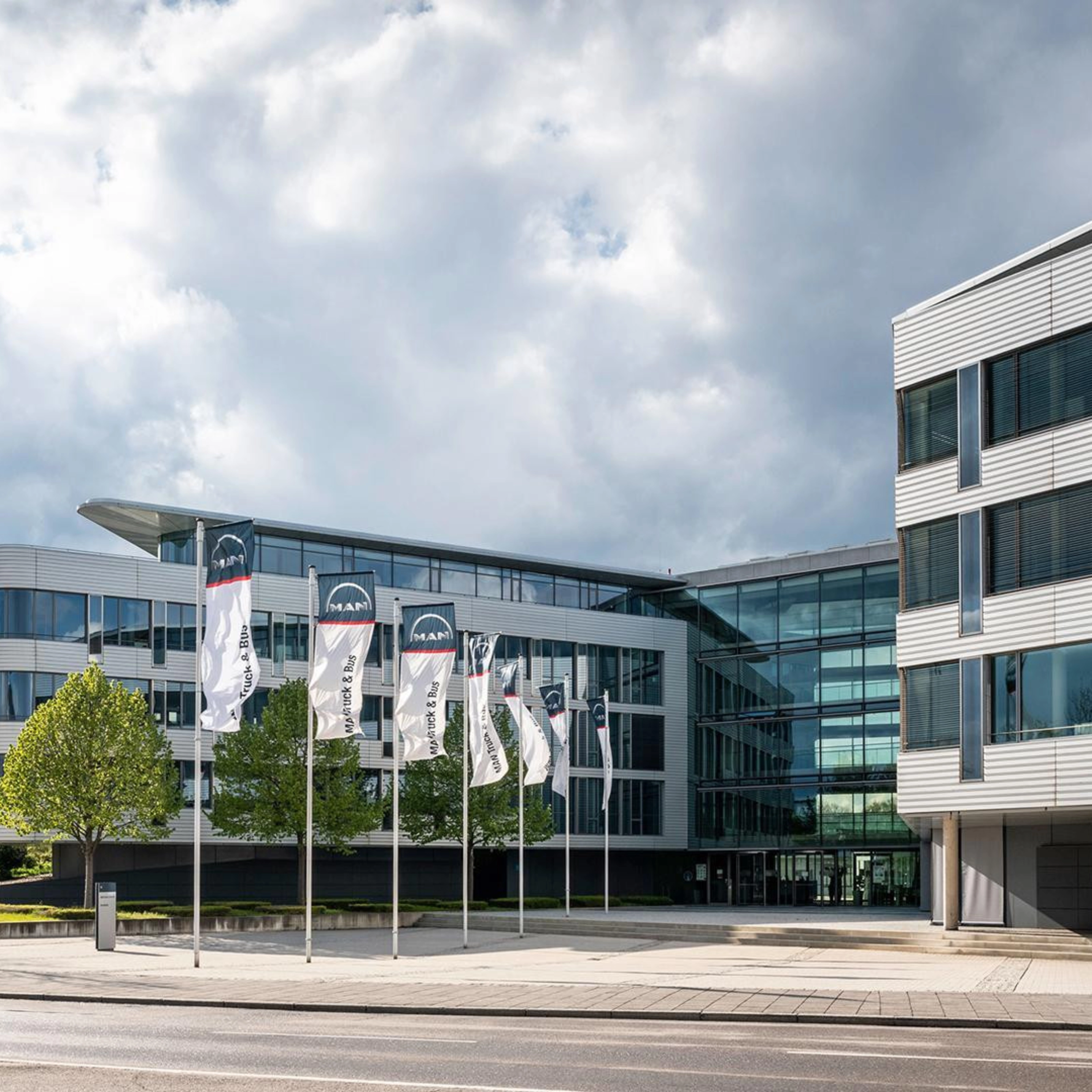 Modern office building with glass facade and MAN Truck & Bus flags in front.