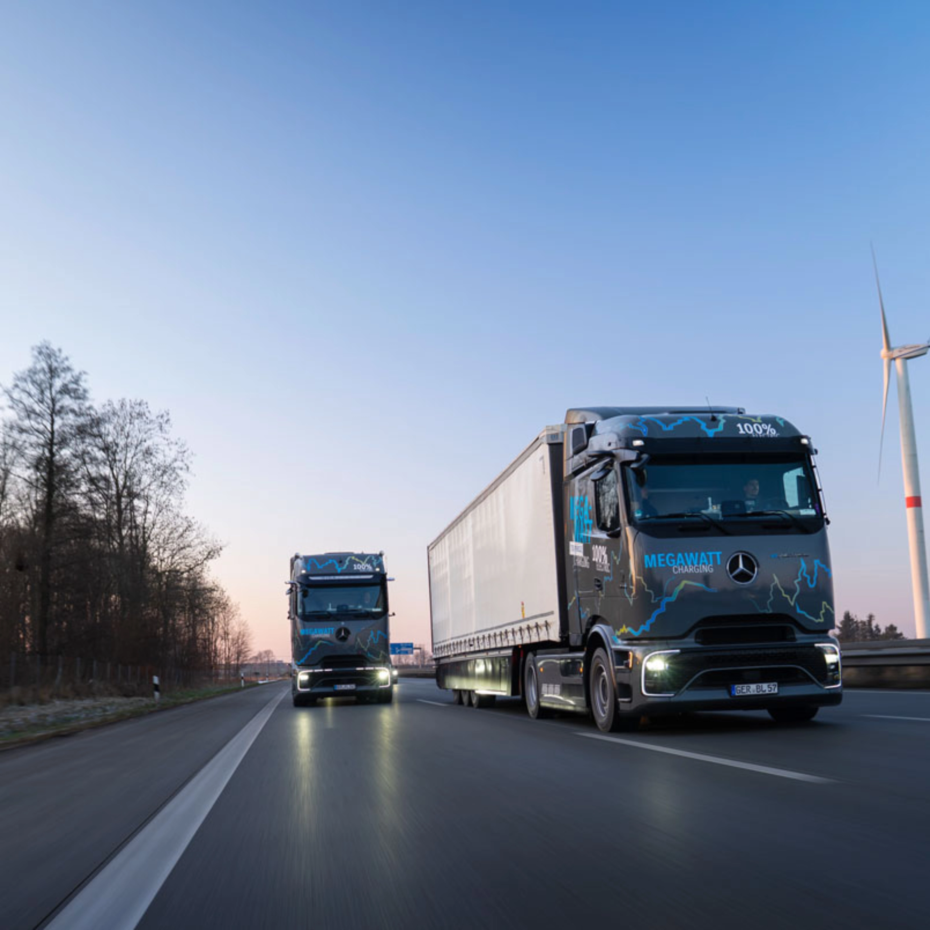 Zwei elektrische Mercedes-Benz-Lkw mit „Megawatt Charging“-Aufschrift fahren bei Dämmerung auf der Autobahn.