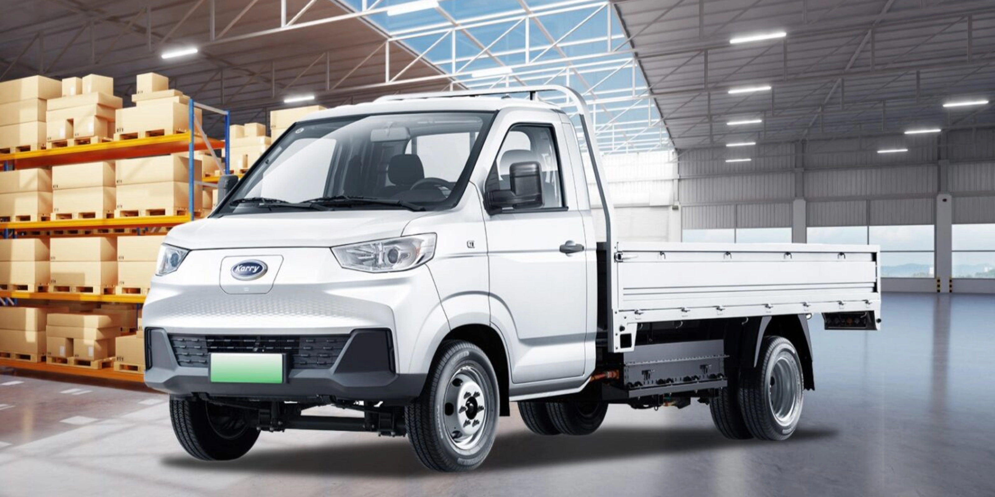 A white Karry electric flatbed truck is parked inside a warehouse near stacked boxes.
