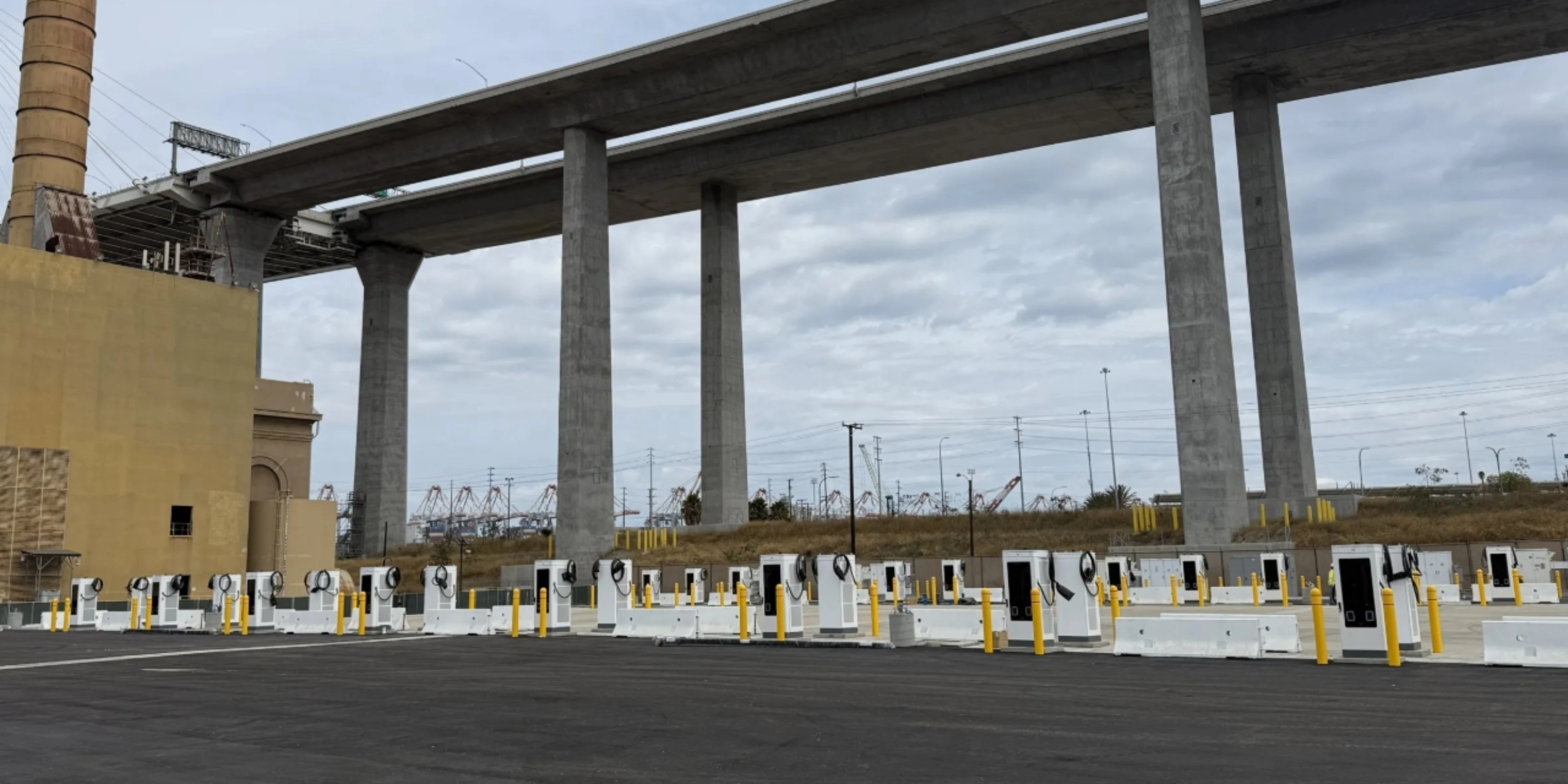 Mehrere E-Ladestationen auf einem Parkplatz unter einer Autobahnbrücke.