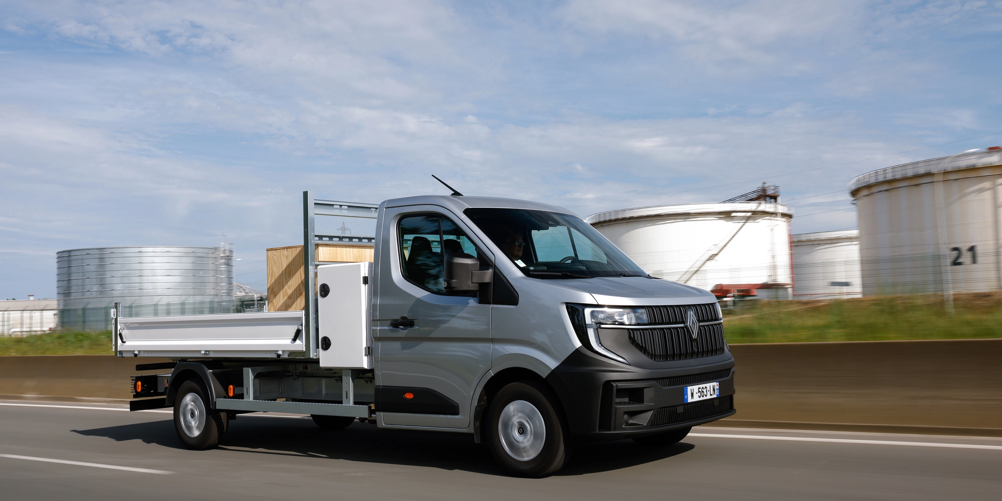 Grey Renault flatbed truck driving on a road in an industrial area.